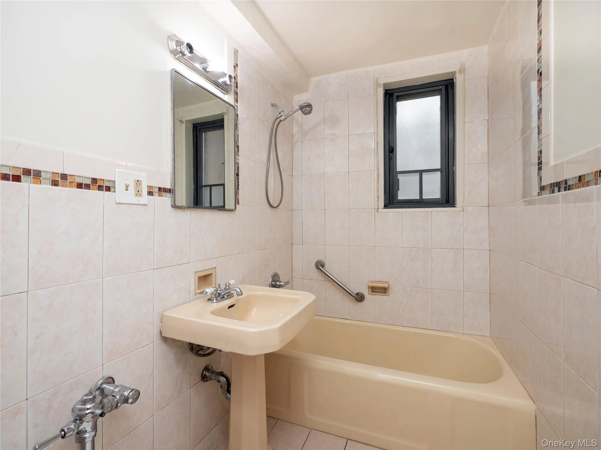 Tiled bathroom featuring a pedestal sink, tub with shower, and a built-in window Tiled bathroom featuring a pedestal sink, tub with shower, and a built-in window