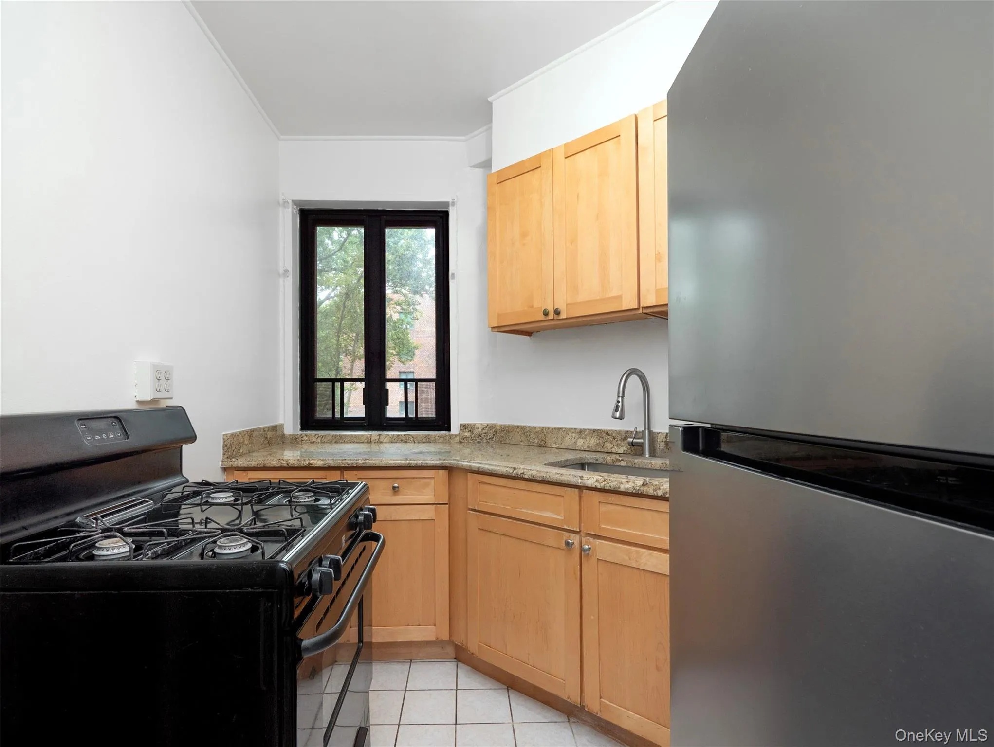 Kitchen featuring granite-style countertops, wood-finish cabinetry, a stainless steel refrigerator, and a gas range Kitchen featuring granite-style countertops, wood-finish cabinetry, a stainless steel refrigerator, and a gas range