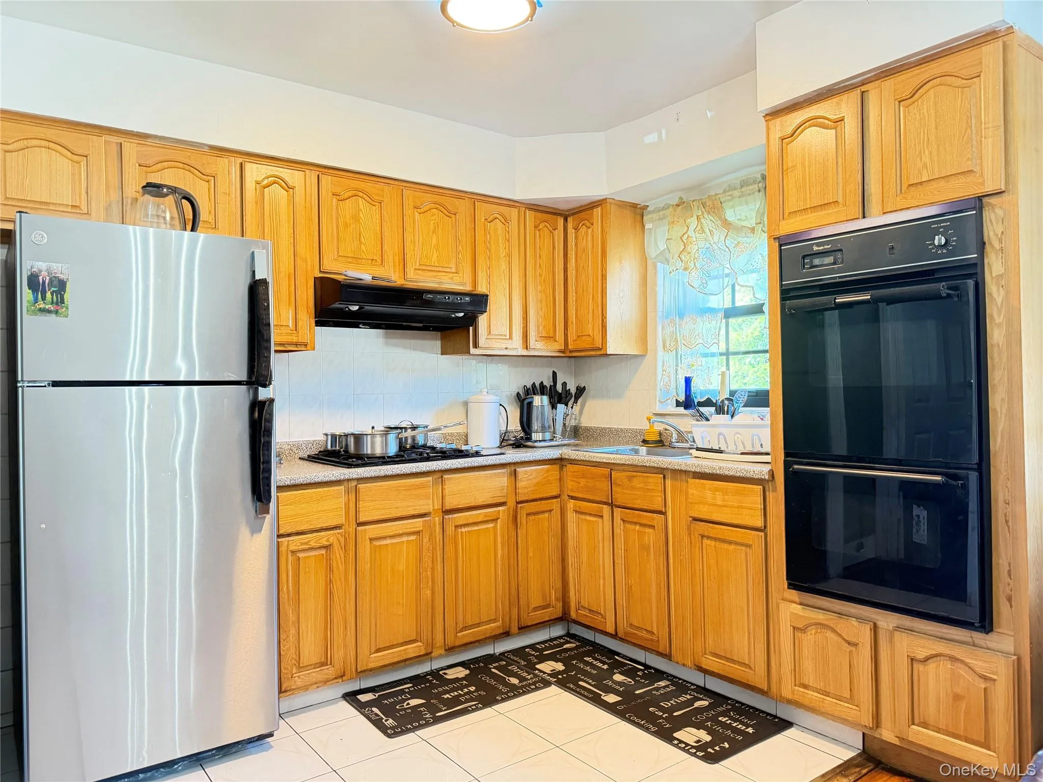 Wood-finish cabinetry, stainless steel refrigerator, built-in double oven, and light-toned countertops Wood-finish cabinetry, stainless steel refrigerator, built-in double oven, and light-toned countertops