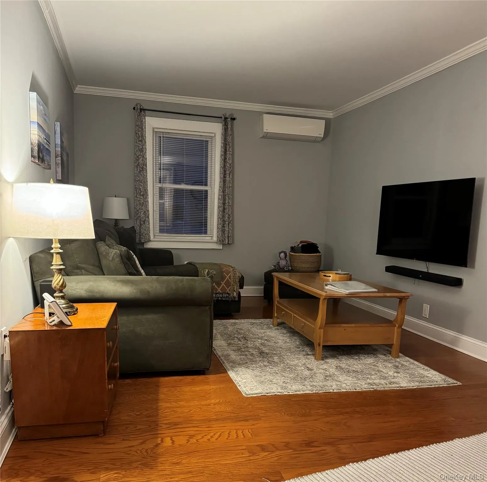 Living area with crown molding, wood finished floors, and a wall unit AC Living area with crown molding, wood finished floors, and a wall unit AC