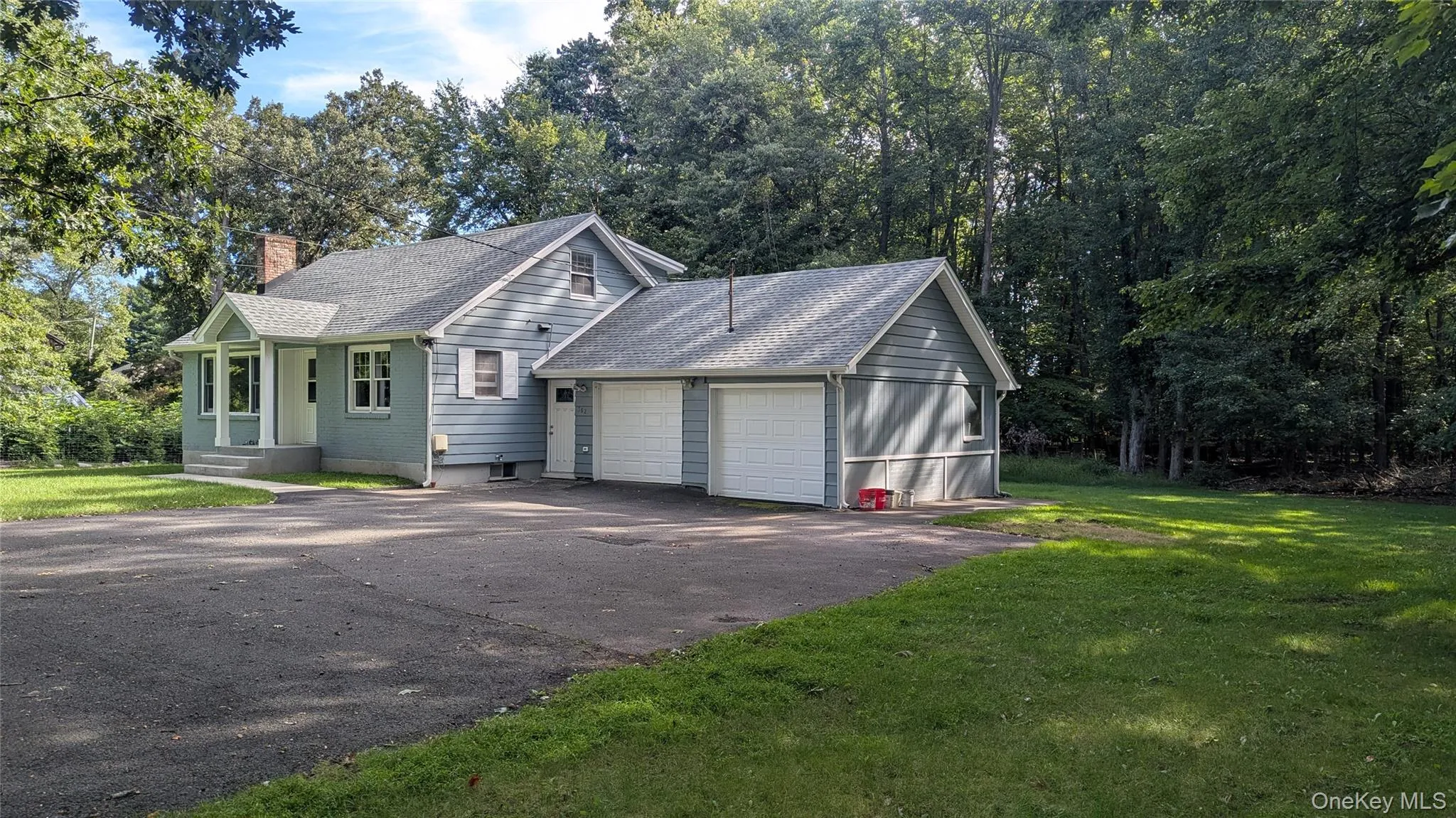 Residential structure featuring light blue siding, a two-car garage, an asphalt driveway, and surrounding mature trees Residential structure featuring light blue siding, a two-car garage, an asphalt driveway, and surrounding mature trees