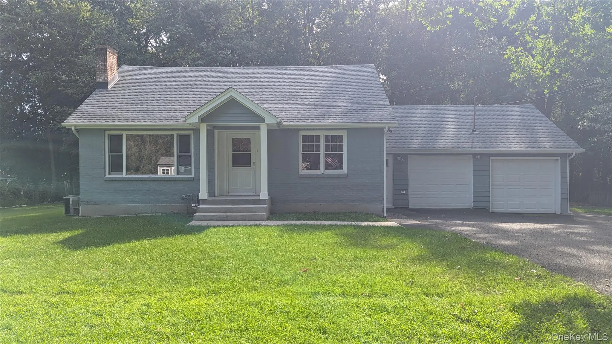 Light blue siding exterior with a dark shingle roof, featuring a covered entry, multiple windows, and an attached two-car garage Light blue siding exterior with a dark shingle roof, featuring a covered entry, multiple windows, and an attached two-car garage