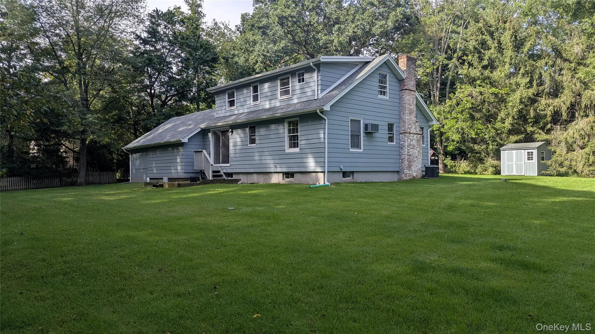 Expansive green lawn with a blue siding exterior, a prominent brick chimney, and a detached storage shed Expansive green lawn with a blue siding exterior, a prominent brick chimney, and a detached storage shed