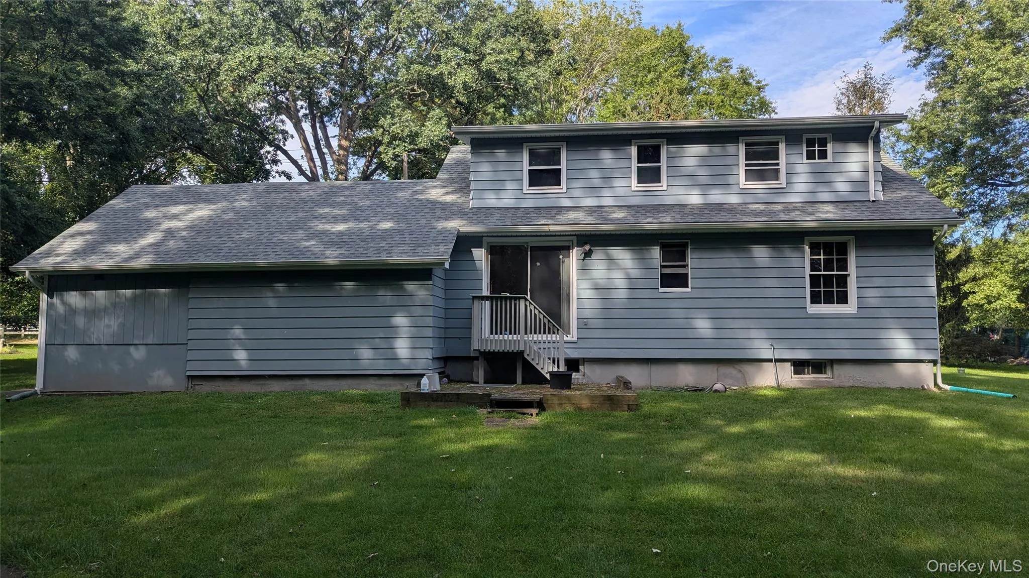 Exterior featuring a large grassy area, light blue siding, white trim windows, and a rear deck with steps Exterior featuring a large grassy area, light blue siding, white trim windows, and a rear deck with steps
