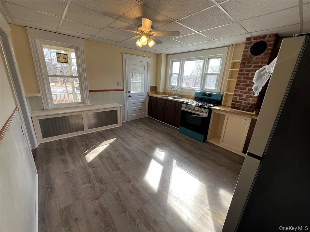 Bright, open kitchen featuring wood-finish flooring, black appliances, cream cabinetry, and exposed brick accents Bright, open kitchen featuring wood-finish flooring, black appliances, cream cabinetry, and exposed brick accents