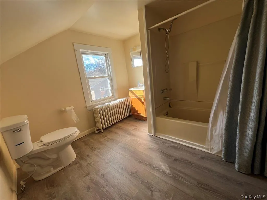 Full bathroom featuring wood-finish flooring, a window, and a bathtub with an integrated shower Full bathroom featuring wood-finish flooring, a window, and a bathtub with an integrated shower