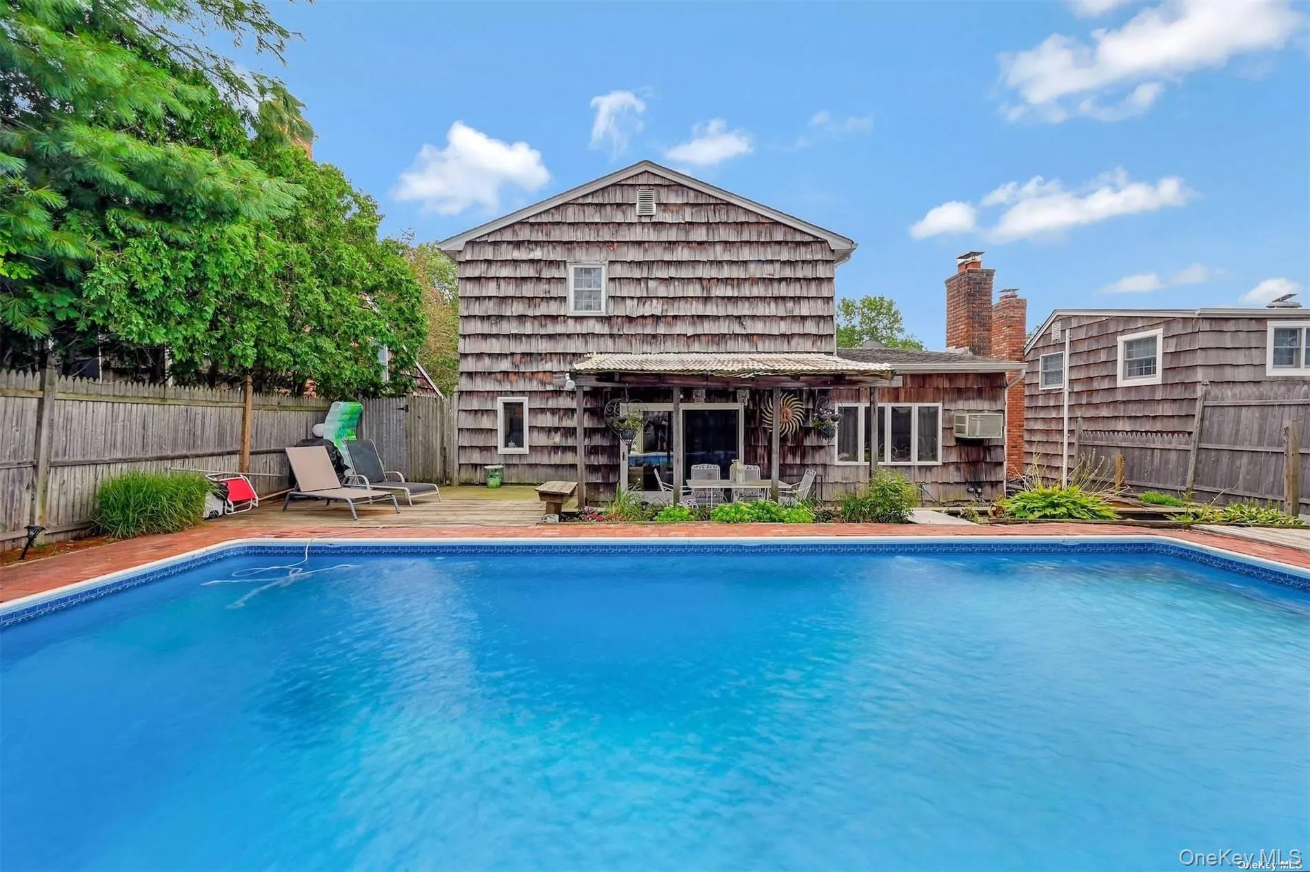 In-ground swimming pool with brick coping, shingle-sided exterior, wood privacy fence, and multiple brick chimneys In-ground swimming pool with brick coping, shingle-sided exterior, wood privacy fence, and multiple brick chimneys