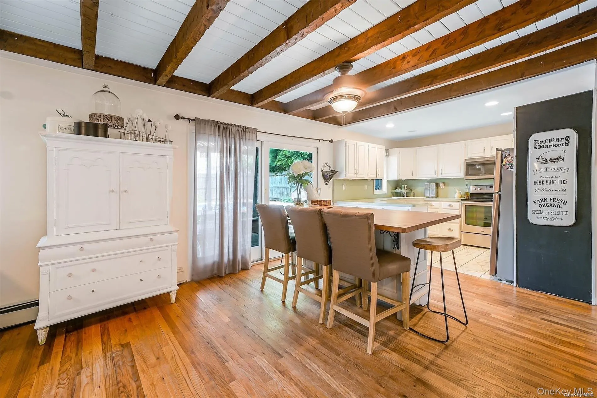 Exposed wood beams, ceiling fan with integrated lighting, wood-finish flooring, white cabinetry, and stainless steel appliances Exposed wood beams, ceiling fan with integrated lighting, wood-finish flooring, white cabinetry, and stainless steel appliances