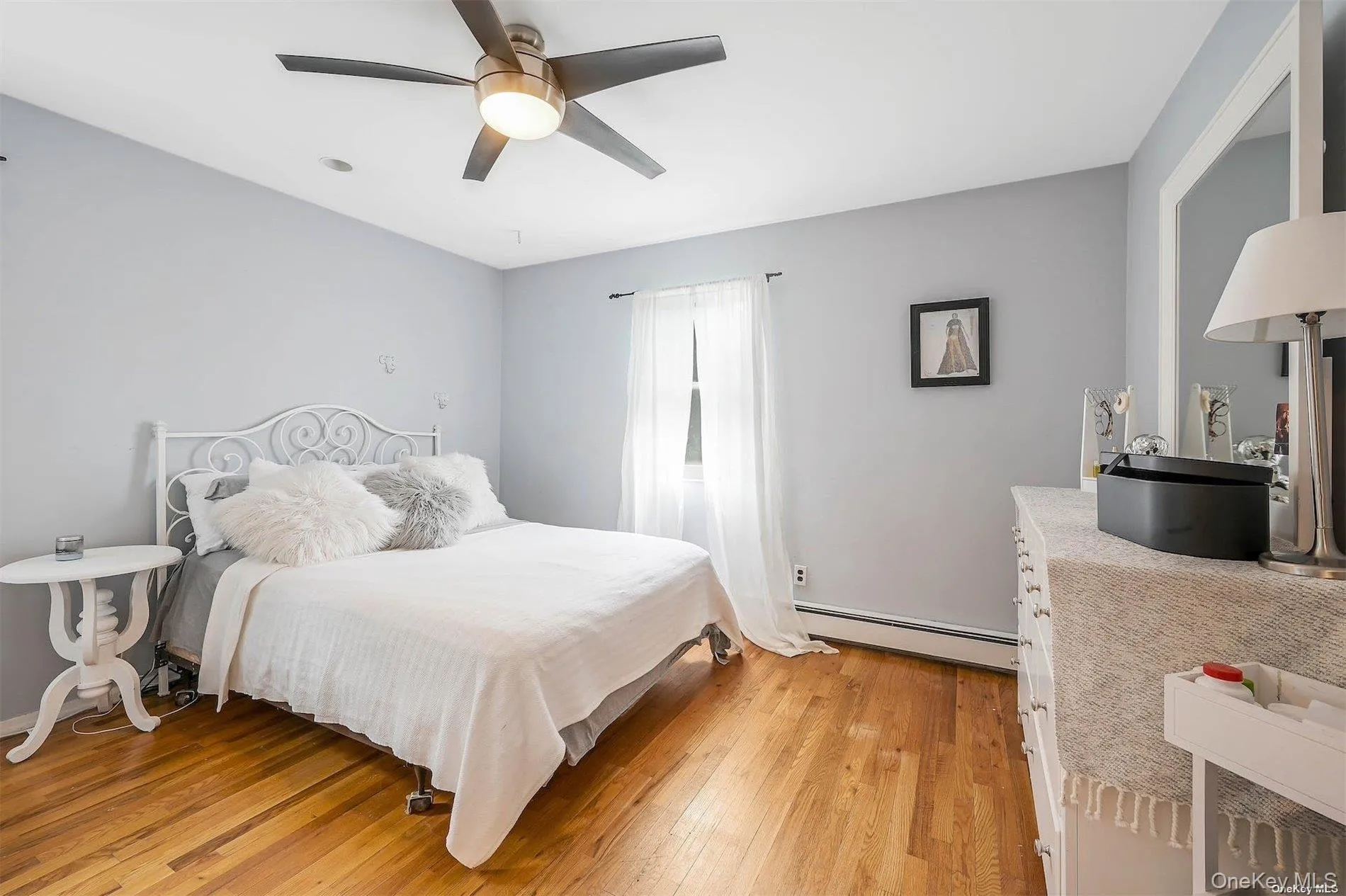 Hardwood flooring, ceiling fan with integrated lighting, window with curtain rod, baseboard heating, and a built-in mirror Hardwood flooring, ceiling fan with integrated lighting, window with curtain rod, baseboard heating, and a built-in mirror