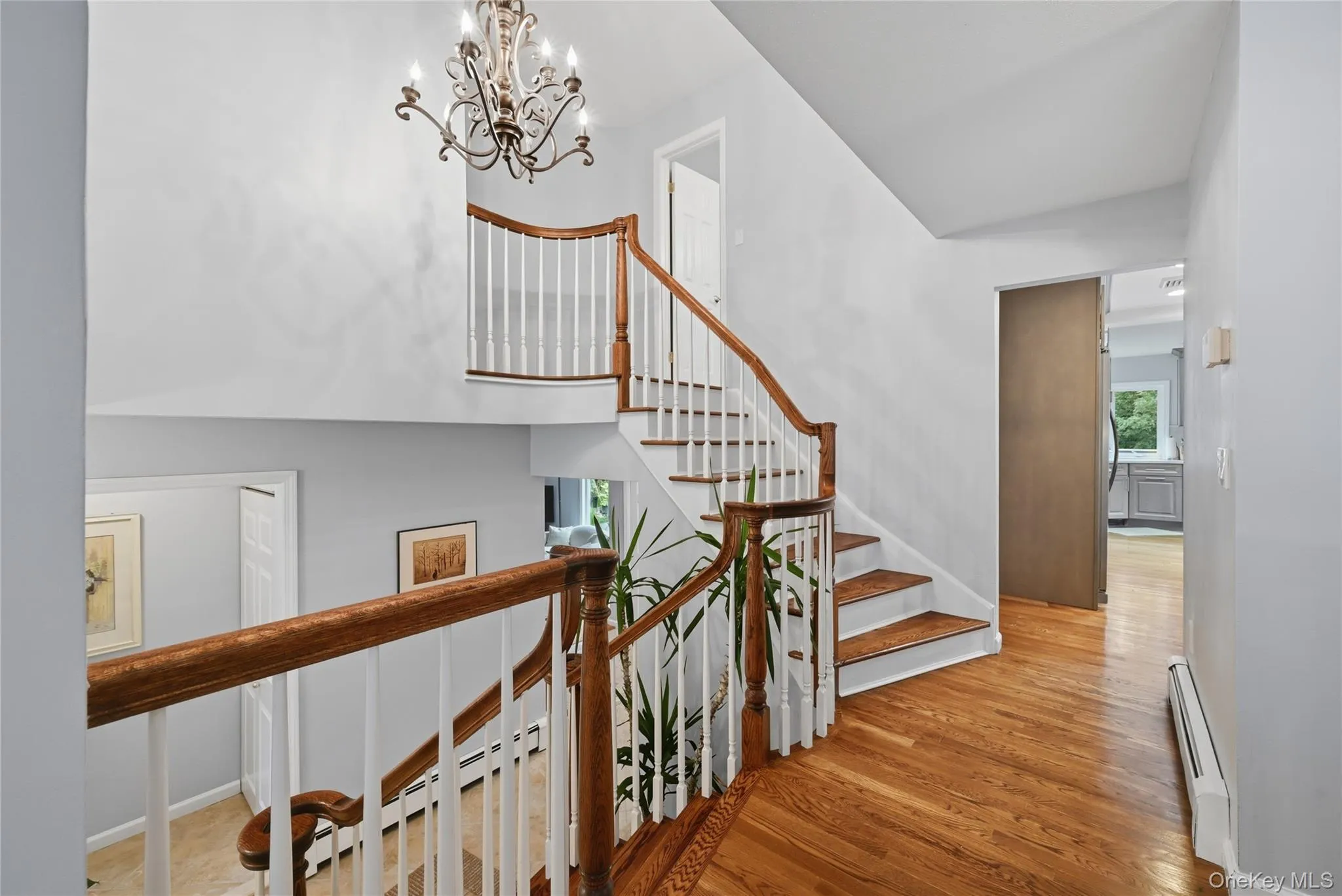 Entry with wood-finish flooring, a traditional chandelier, and a curved staircase with wood handrails and white balusters Entry with wood-finish flooring, a traditional chandelier, and a curved staircase with wood handrails and white balusters