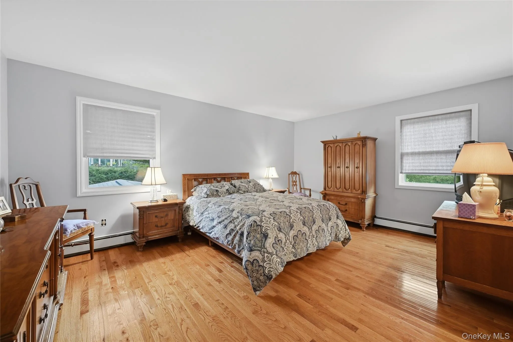 Primary bedroom. Hardwood flooring, light gray wall finish, white trim, and two windows Primary bedroom. Hardwood flooring, light gray wall finish, white trim, and two windows