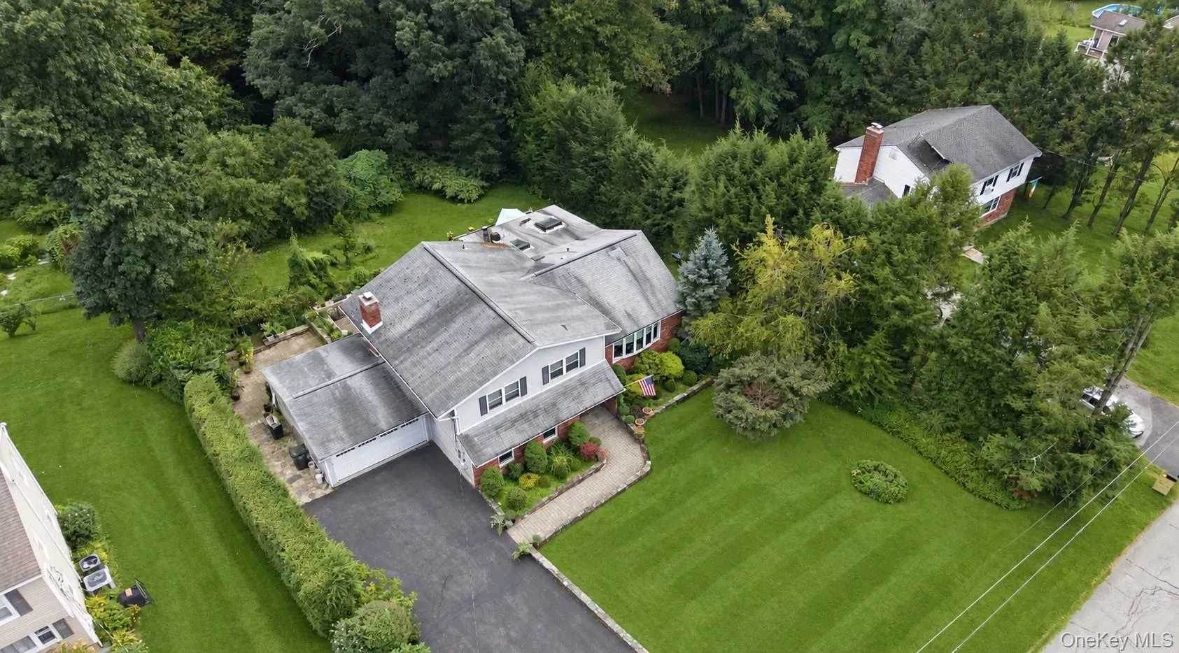 Expansive grounds featuring a large paved driveway, mature landscaping, and a brick facade Expansive grounds featuring a large paved driveway, mature landscaping, and a brick facade