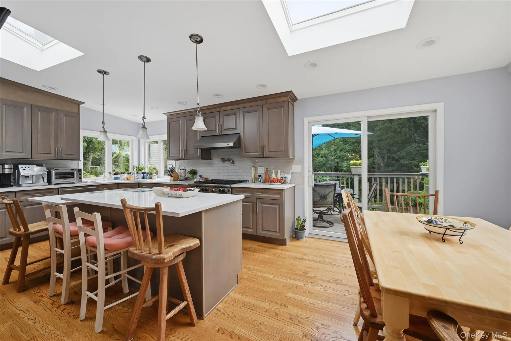 Kitchen featuring skylights, wood-finish flooring, shaker-style cabinetry, a central island with countertop, and a sliding glass door to an exterior deck Kitchen featuring skylights, wood-finish flooring, shaker-style cabinetry, a central island with countertop, and a sliding glass door to an exterior deck