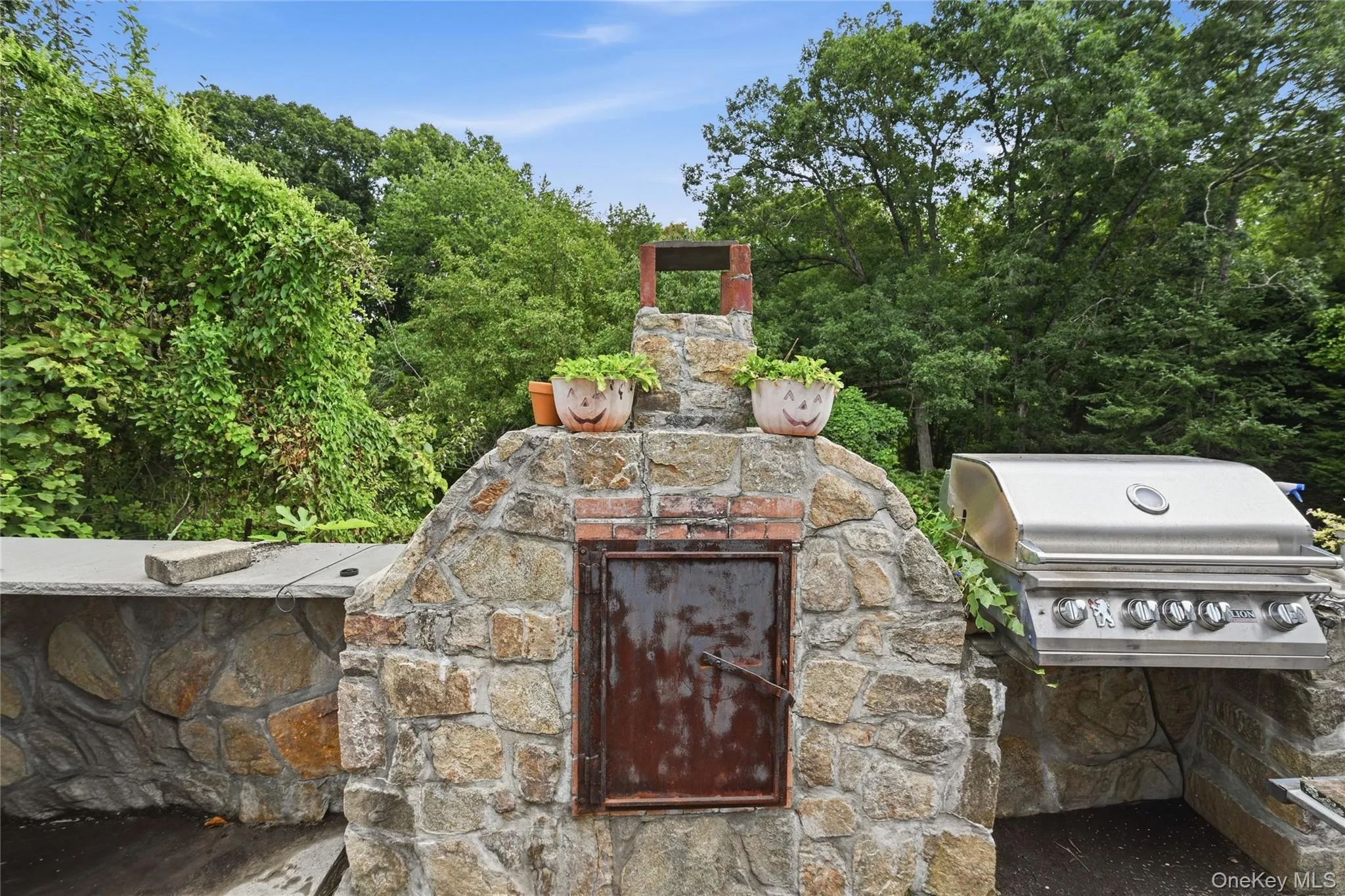 Outdoor stone oven, stone countertop, built-in grill, and abundant surrounding greenery Outdoor stone oven, stone countertop, built-in grill, and abundant surrounding greenery