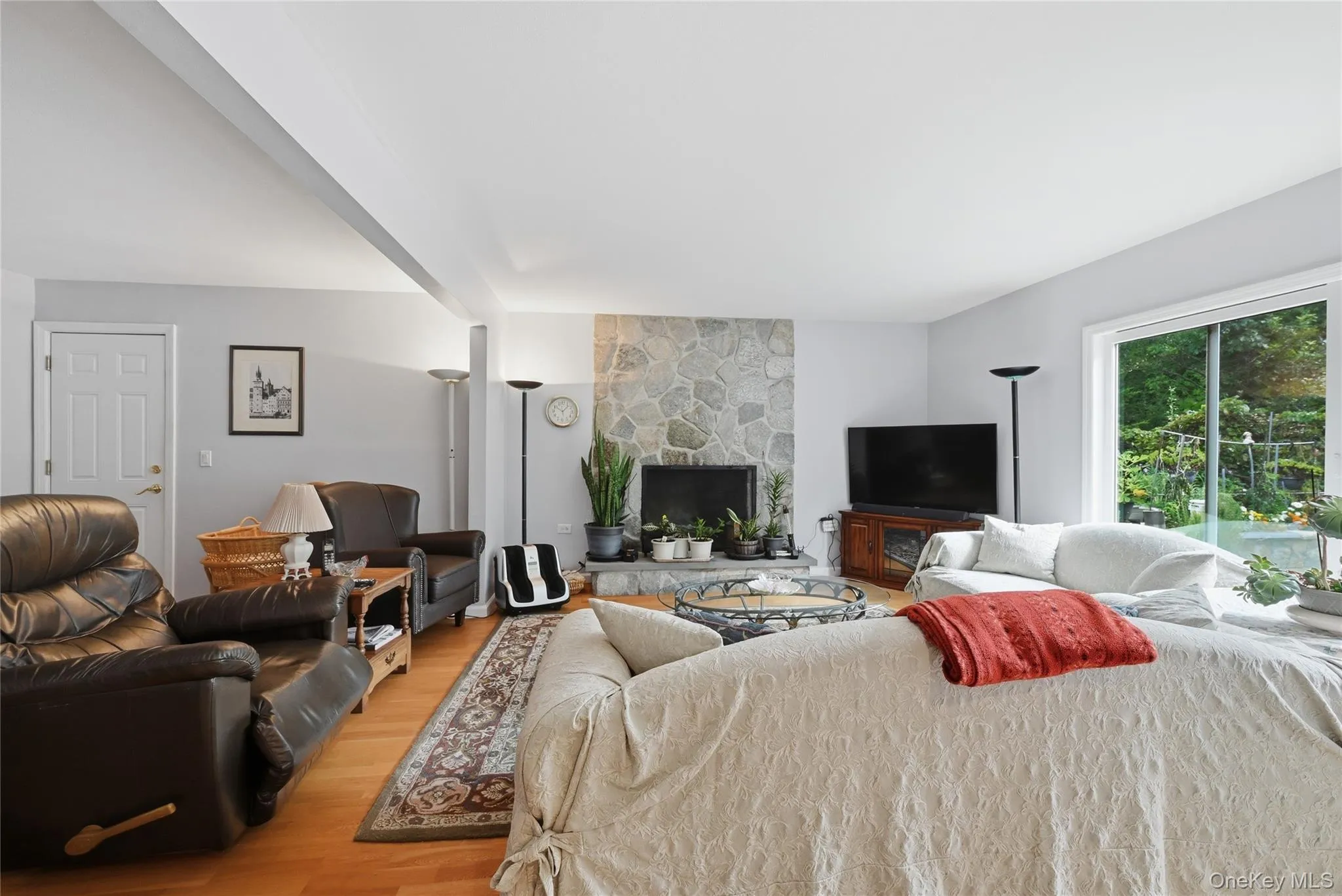 Living area featuring a stone-clad fireplace, light wood-finish flooring, and a large sliding glass door Living area featuring a stone-clad fireplace, light wood-finish flooring, and a large sliding glass door