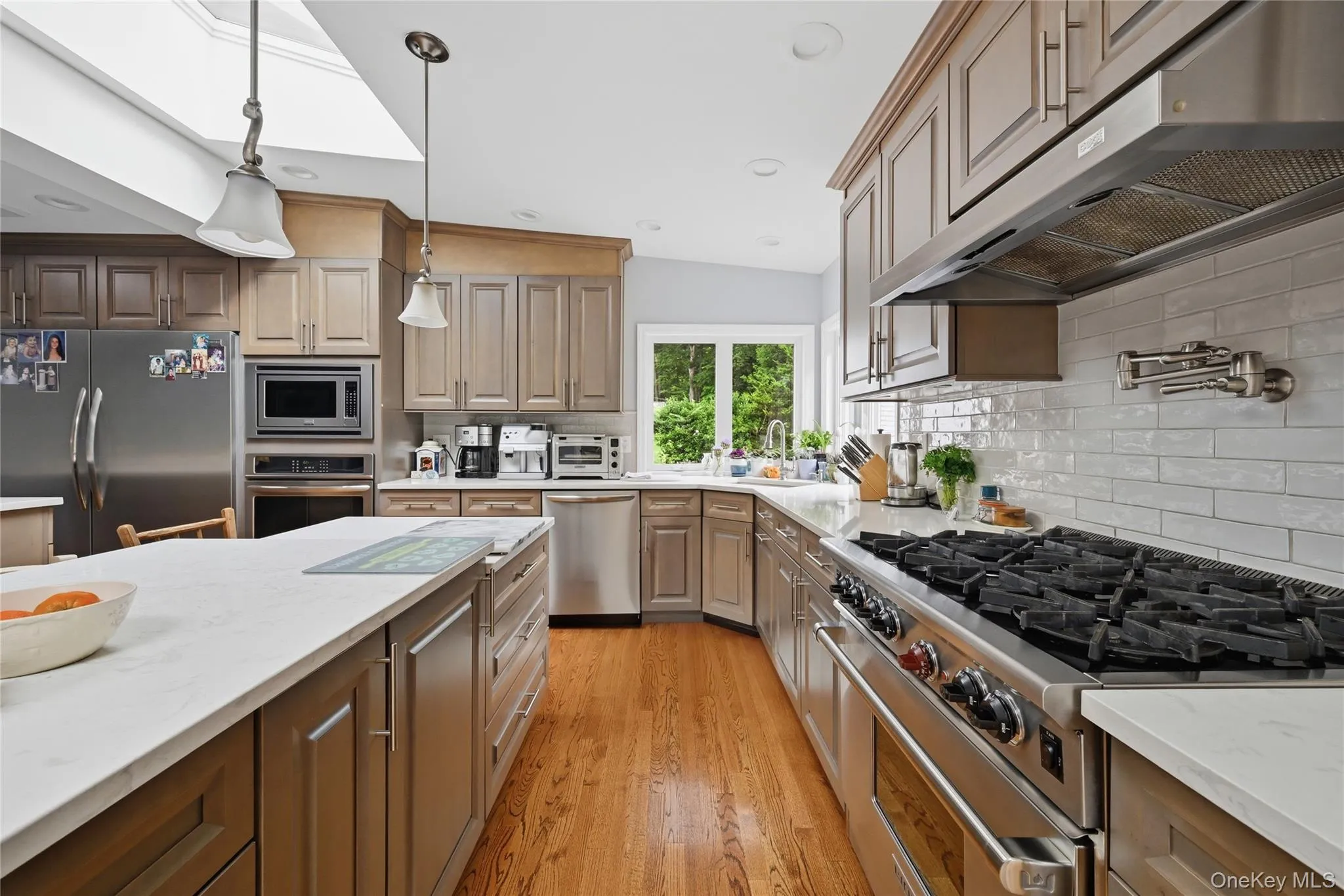 Well-appointed kitchen featuring hardwood flooring, stainless steel appliances, white subway tile backsplash, and a large center island with a light-colored countertop Well-appointed kitchen featuring hardwood flooring, stainless steel appliances, white subway tile backsplash, and a large center island with a light-colored countertop