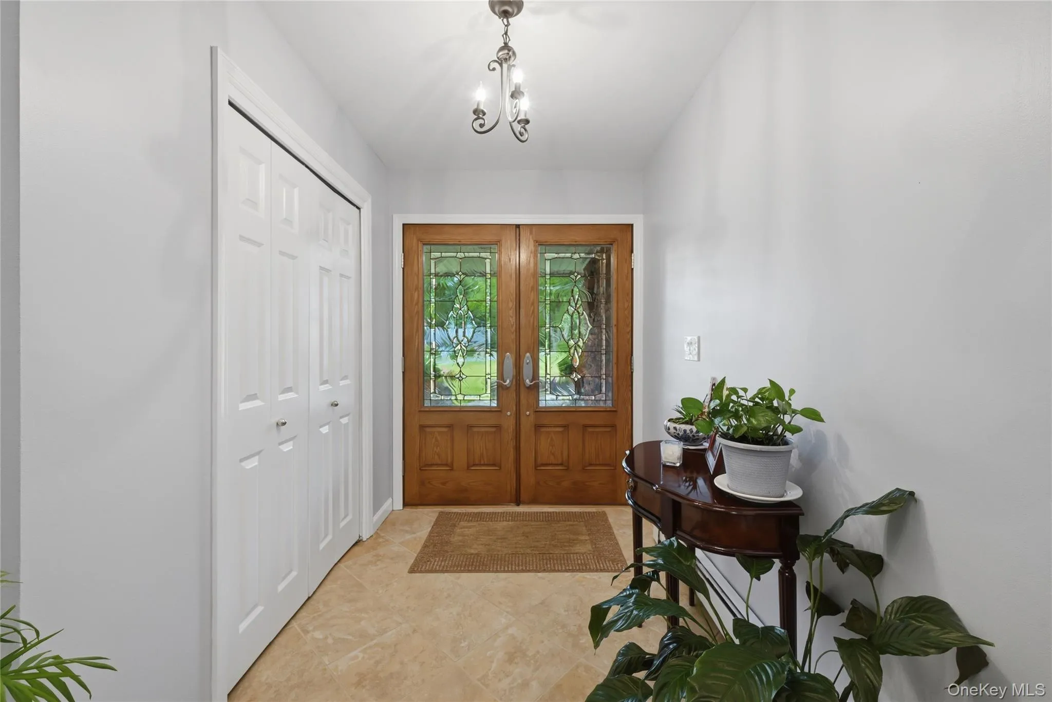 Double wood-finish entry doors with decorative glass inserts, tile flooring, and a white bi-fold closet Double wood-finish entry doors with decorative glass inserts, tile flooring, and a white bi-fold closet