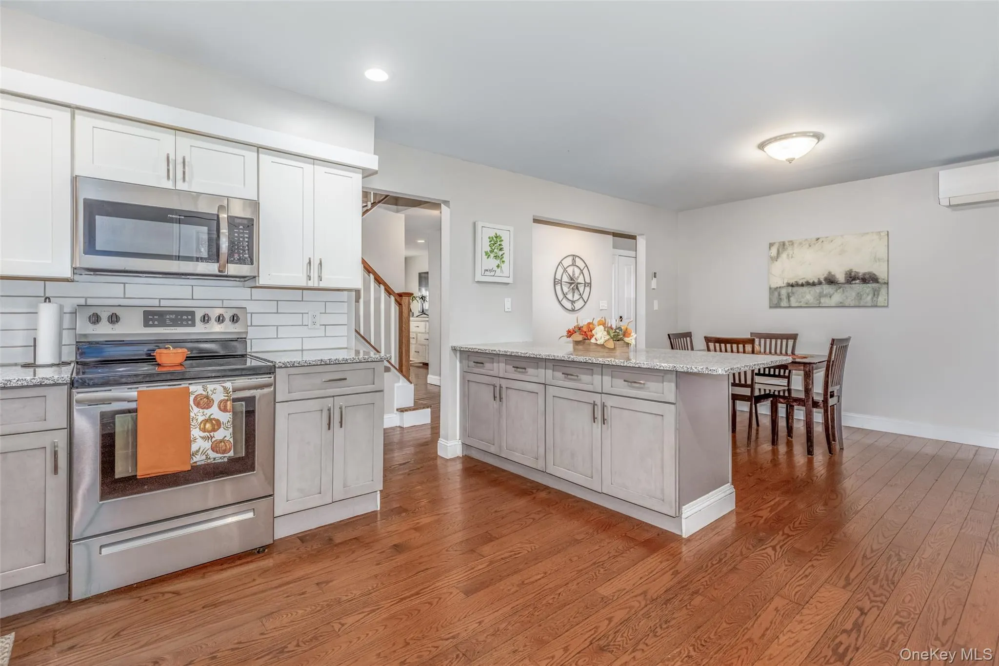 Kitchen featuring a center island, wood-finish flooring, stainless steel appliances, a subway tile backsplash, and light-toned cabinetry Kitchen featuring a center island, wood-finish flooring, stainless steel appliances, a subway tile backsplash, and light-toned cabinetry