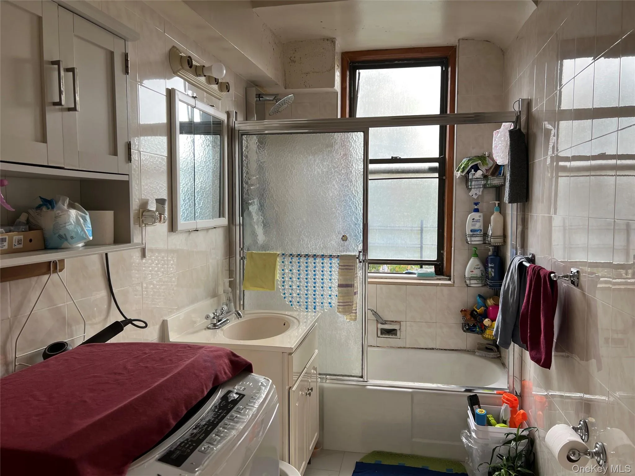 Bathroom with tiled shower / bath combo, vanity, tile walls, washer / dryer, and light tile patterned flooring Bathroom with tiled shower / bath combo, vanity, tile walls, washer / dryer, and light tile patterned flooring