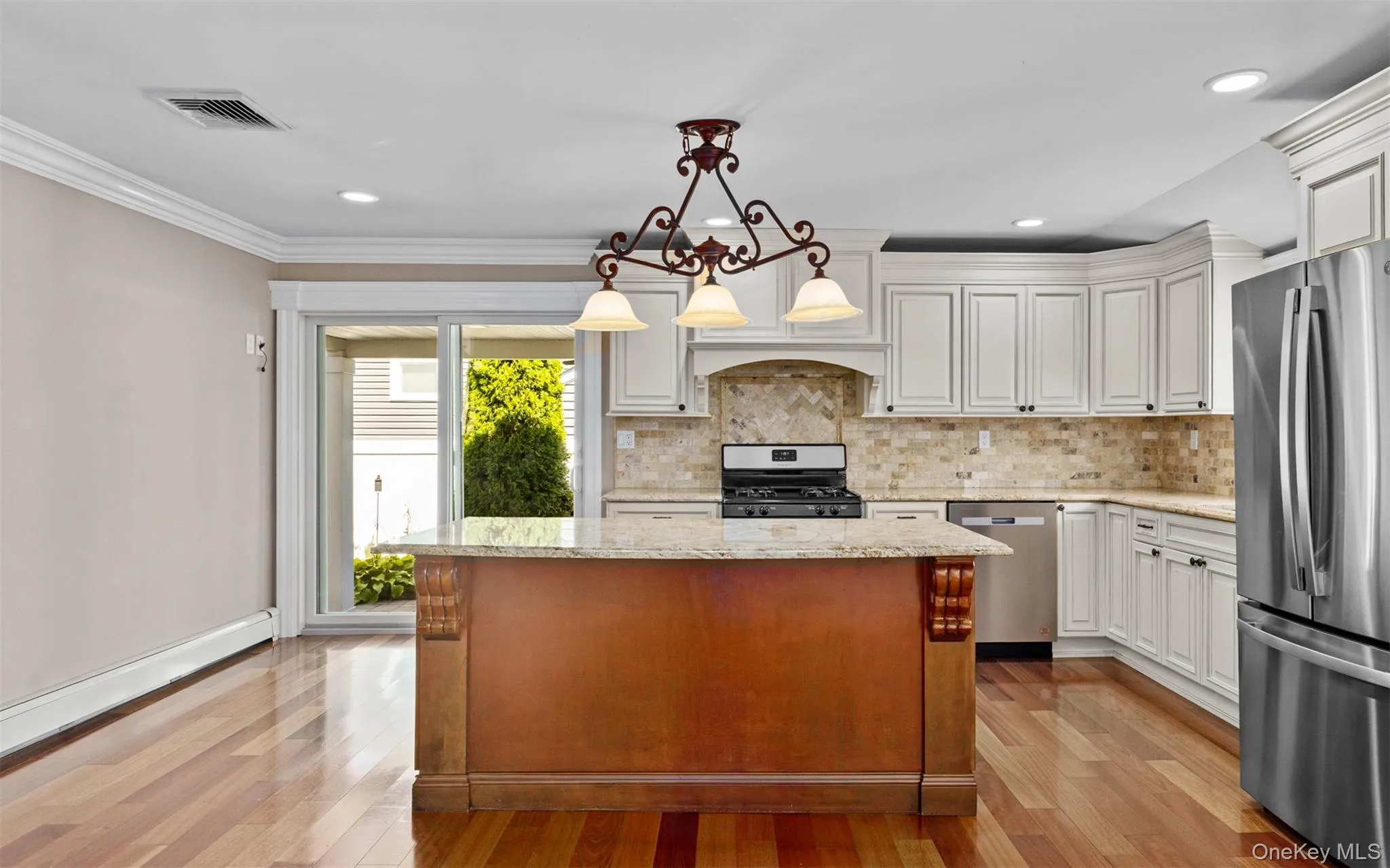 Kitchen featuring a central island with carved accents, stainless steel appliances, light-toned cabinetry, and wood-finish flooring Kitchen featuring a central island with carved accents, stainless steel appliances, light-toned cabinetry, and wood-finish flooring