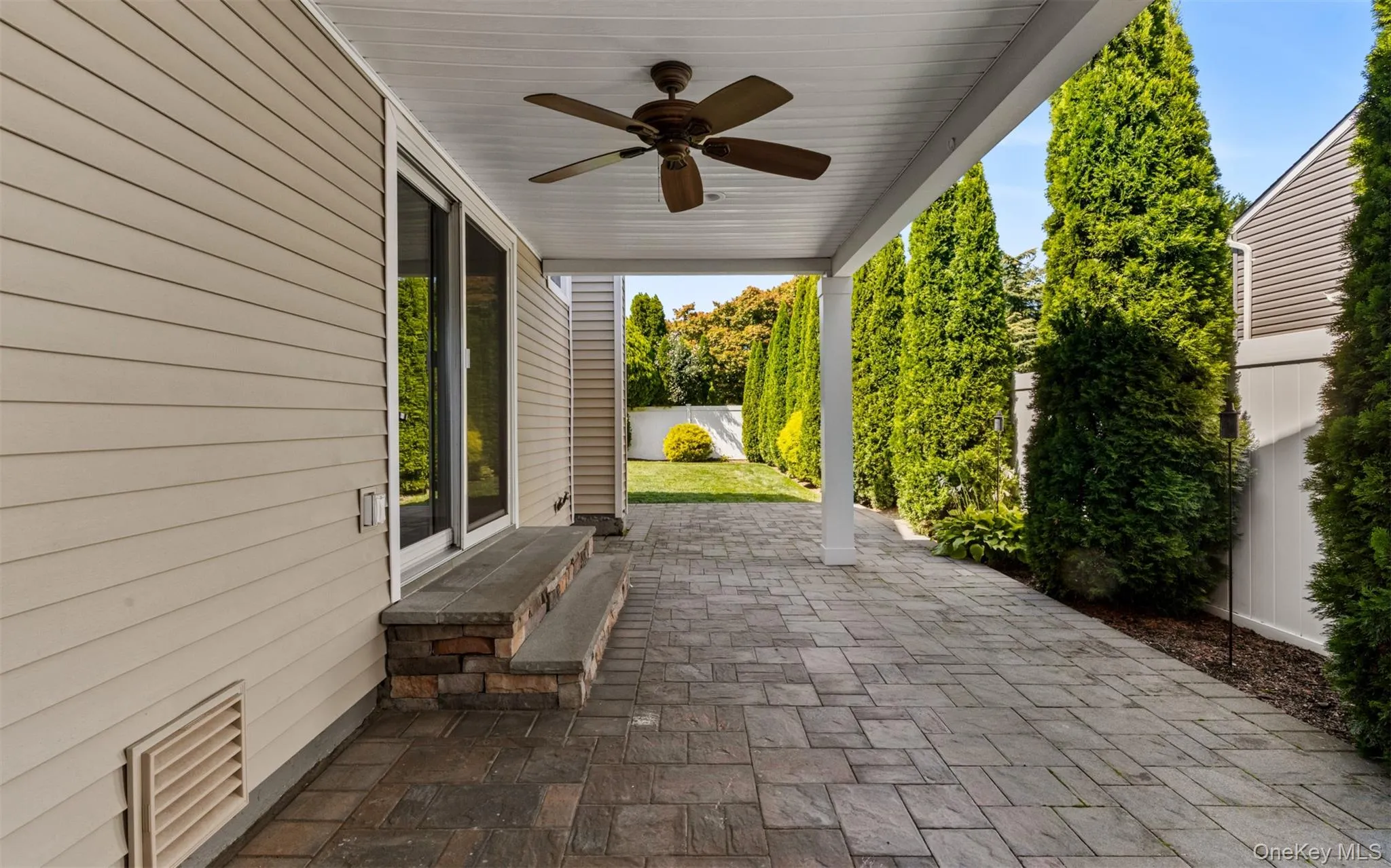 Covered patio featuring a ceiling fan, paver flooring, sliding glass doors, and privacy landscaping Covered patio featuring a ceiling fan, paver flooring, sliding glass doors, and privacy landscaping