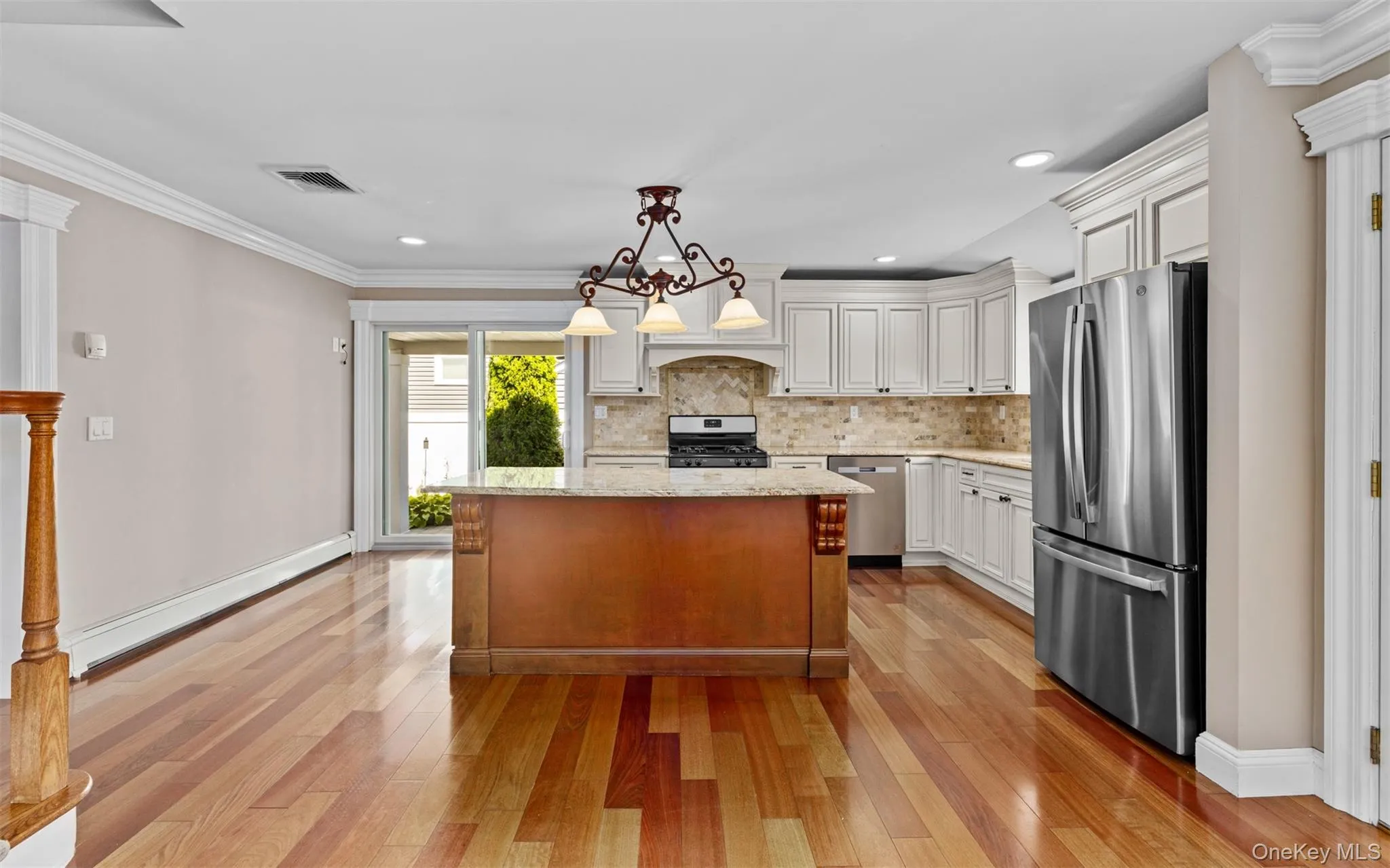 Hardwood flooring throughout, white cabinetry with crown molding, stainless steel appliances, a kitchen island with a stone countertop, and glass sliding doors Hardwood flooring throughout, white cabinetry with crown molding, stainless steel appliances, a kitchen island with a stone countertop, and glass sliding doors