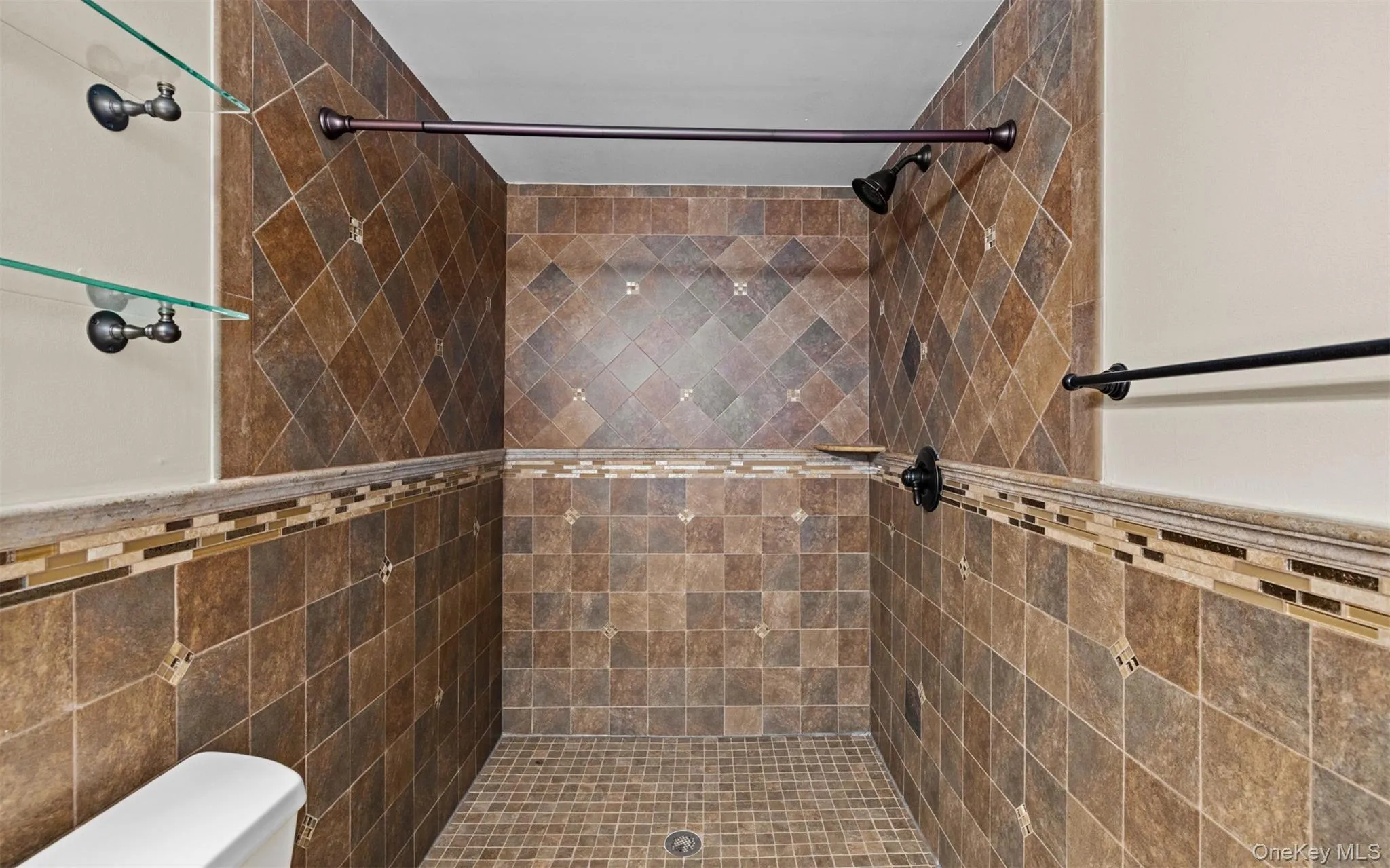 Tiled shower enclosure featuring a mosaic accent band, integrated showerhead, and glass shelving Tiled shower enclosure featuring a mosaic accent band, integrated showerhead, and glass shelving