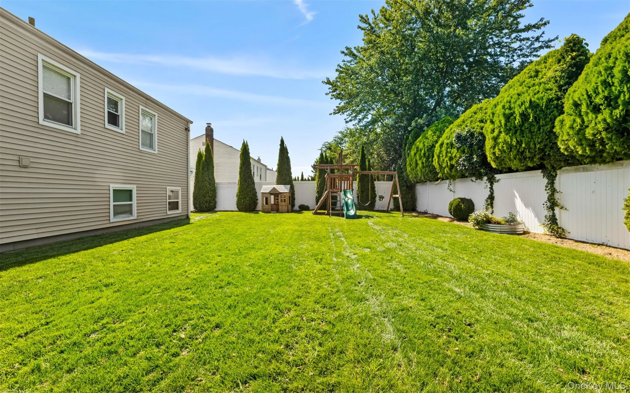 Expansive green lawn with a white privacy fence and mature perimeter plantings Expansive green lawn with a white privacy fence and mature perimeter plantings
