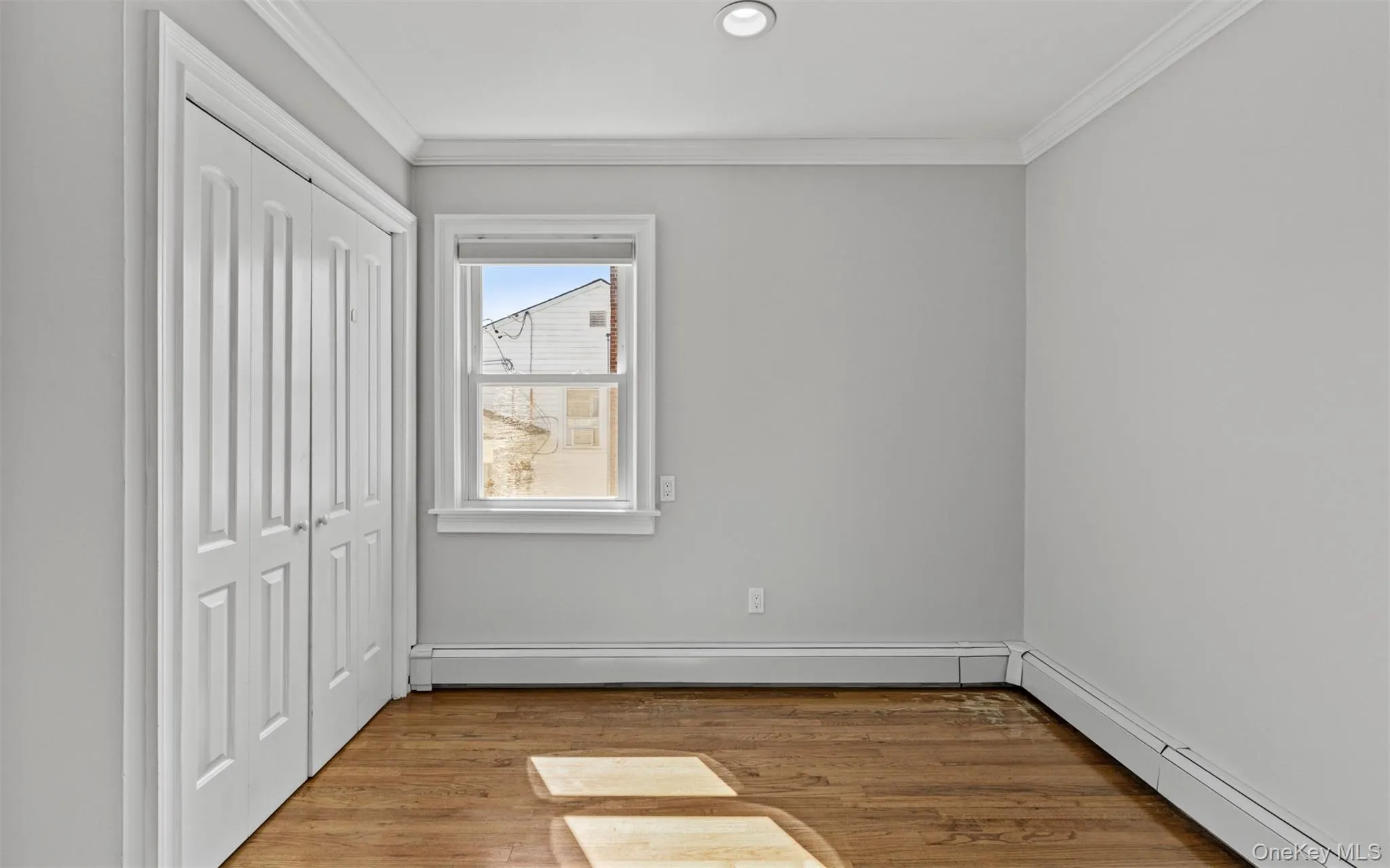 Hardwood flooring, recessed lighting, crown molding, white bi-fold closet doors, and a double-hung window Hardwood flooring, recessed lighting, crown molding, white bi-fold closet doors, and a double-hung window