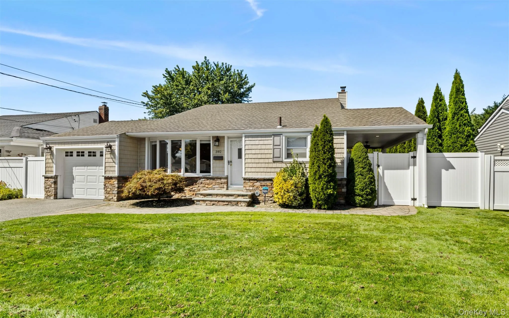 Ranch-style exterior with stone veneer and shingle siding, an attached garage, a covered carport, and a paved driveway Ranch-style exterior with stone veneer and shingle siding, an attached garage, a covered carport, and a paved driveway