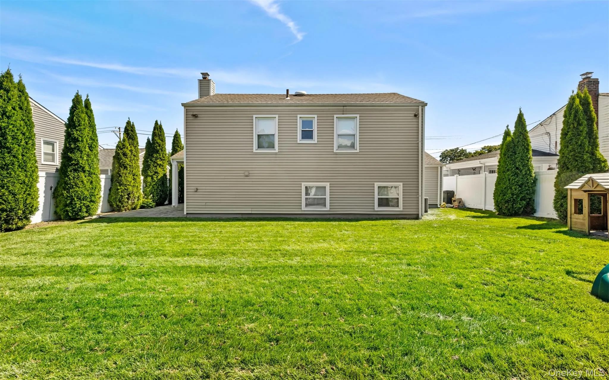 Expansive green lawn with mature evergreen trees and a white privacy fence Expansive green lawn with mature evergreen trees and a white privacy fence