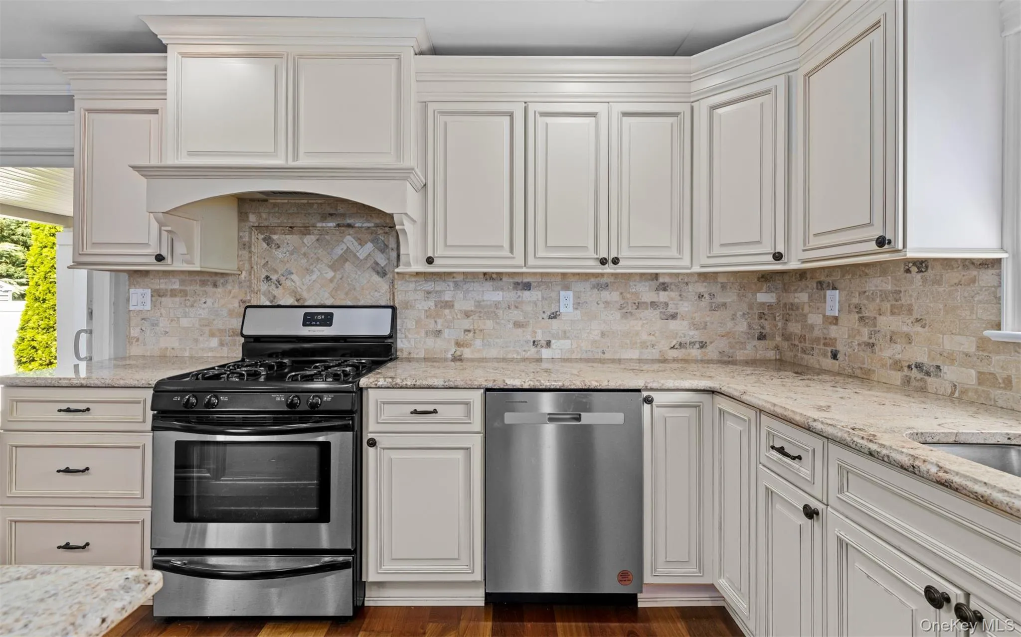Cream-painted cabinetry, stone backsplash, stainless steel appliances, granite countertops, and wood-finish flooring Cream-painted cabinetry, stone backsplash, stainless steel appliances, granite countertops, and wood-finish flooring