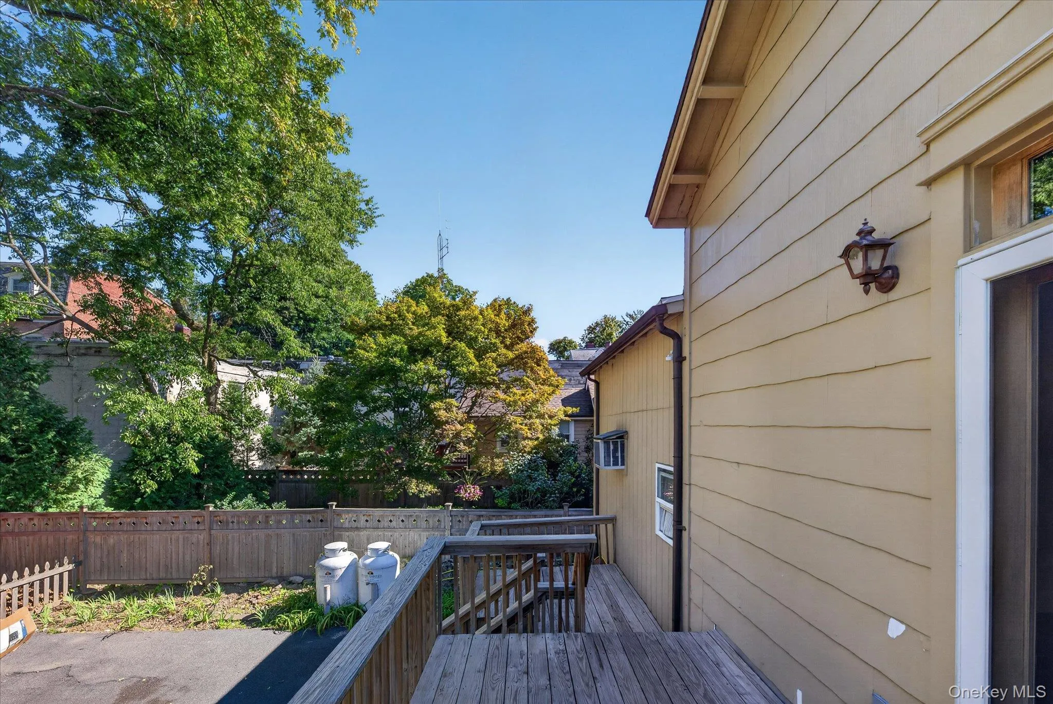 Exterior siding with an attached wall sconce, wooden deck and railings, and surrounding trees Exterior siding with an attached wall sconce, wooden deck and railings, and surrounding trees