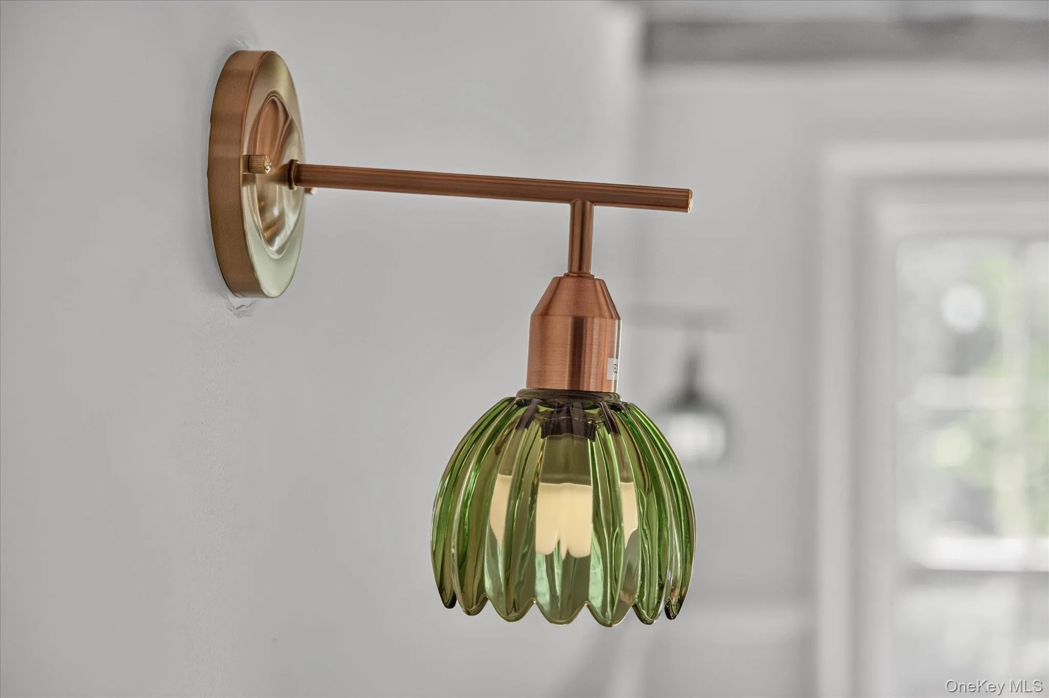 Wall-mounted light fixture featuring a brass-finish backplate, copper-finish arm, and a fluted green glass shade Wall-mounted light fixture featuring a brass-finish backplate, copper-finish arm, and a fluted green glass shade