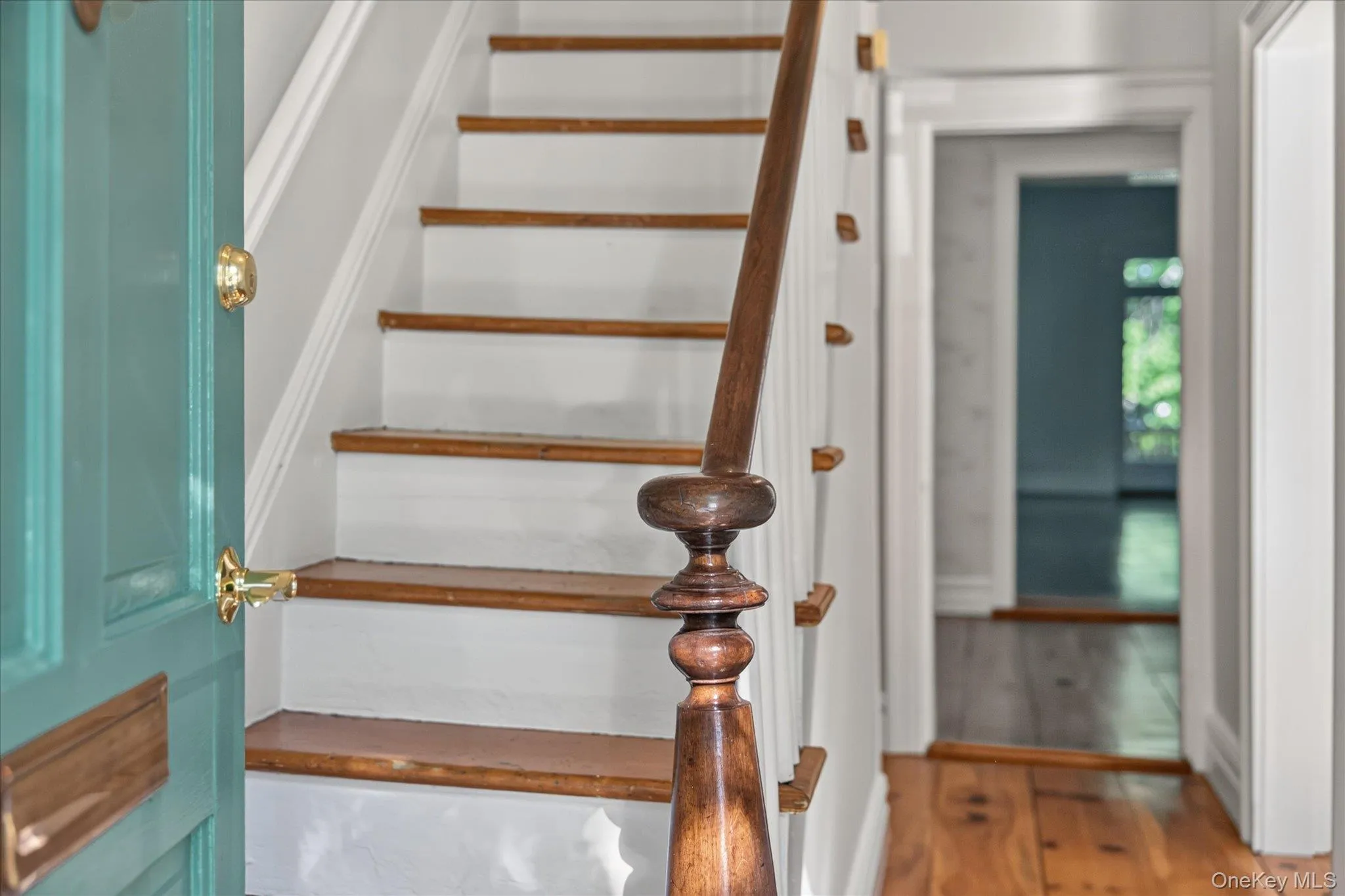 Hardwood flooring, painted risers, wood treads, wood newel post, and a teal door with brass hardware Hardwood flooring, painted risers, wood treads, wood newel post, and a teal door with brass hardware