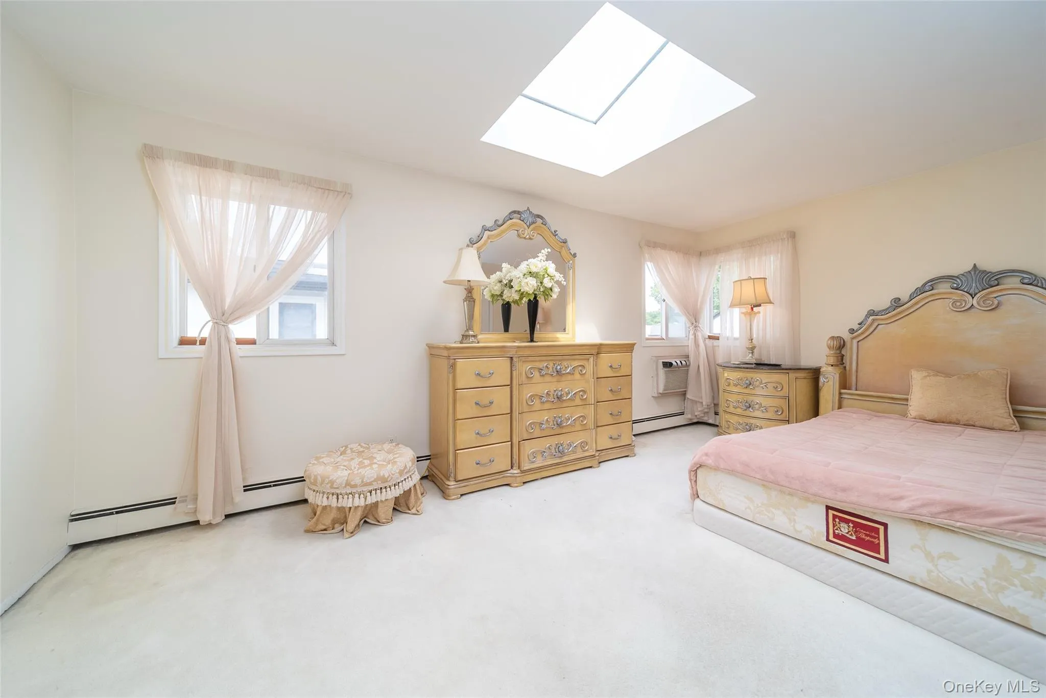 Bedroom featuring a skylight, carpet flooring, a baseboard heating unit, and a wall mounted AC Bedroom featuring a skylight, carpet flooring, a baseboard heating unit, and a wall mounted AC