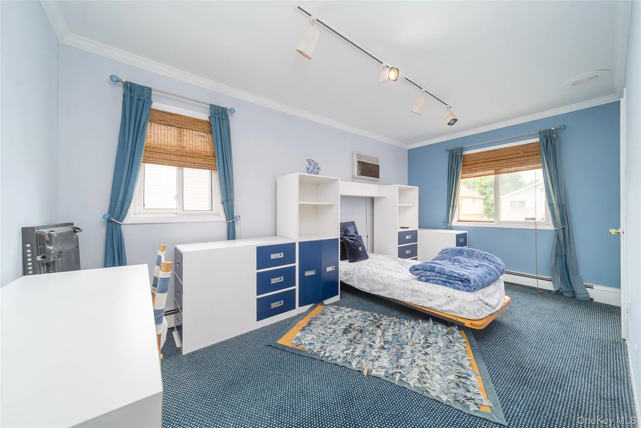 Bedroom featuring carpet, ornamental molding, baseboard heating, track lighting, and a wall mounted air conditioner Bedroom featuring carpet, ornamental molding, baseboard heating, track lighting, and a wall mounted air conditioner