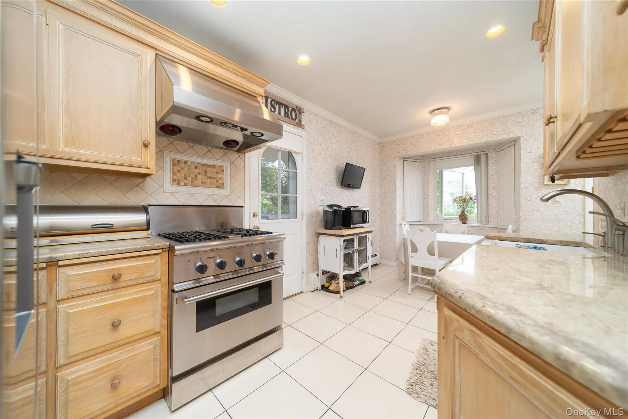 Kitchen with stainless steel stove, ventilation hood, ornamental molding, plenty of natural light, and light brown cabinetry Kitchen with stainless steel stove, ventilation hood, ornamental molding, plenty of natural light, and light brown cabinetry