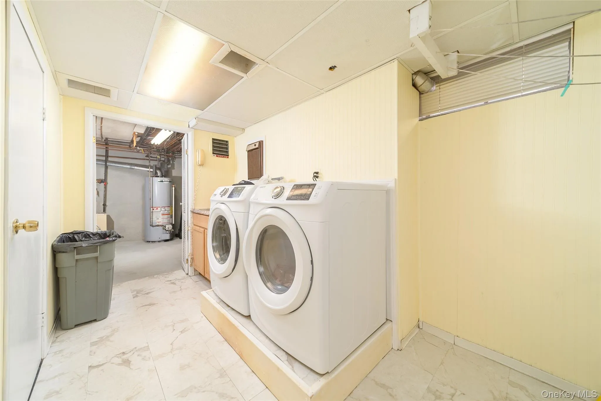 Laundry room featuring washing machine and dryer, water heater, and light marble finish flooring Laundry room featuring washing machine and dryer, water heater, and light marble finish flooring