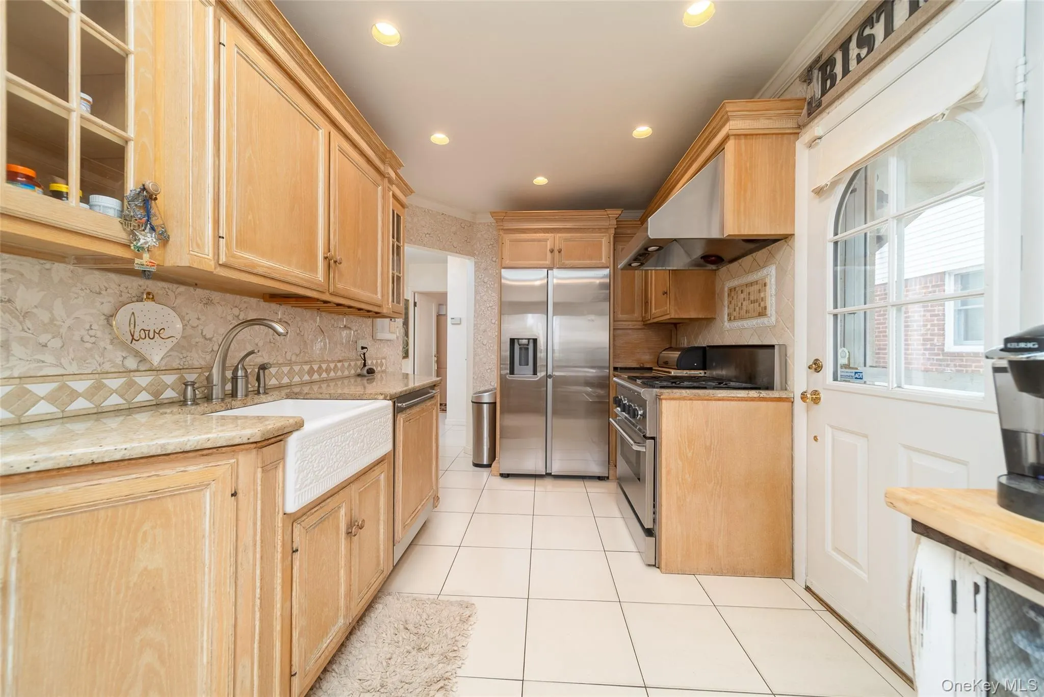 Kitchen featuring appliances with stainless steel finishes, light brown cabinetry, range hood, light tile patterned flooring, and recessed lighting Kitchen featuring appliances with stainless steel finishes, light brown cabinetry, range hood, light tile patterned flooring, and recessed lighting