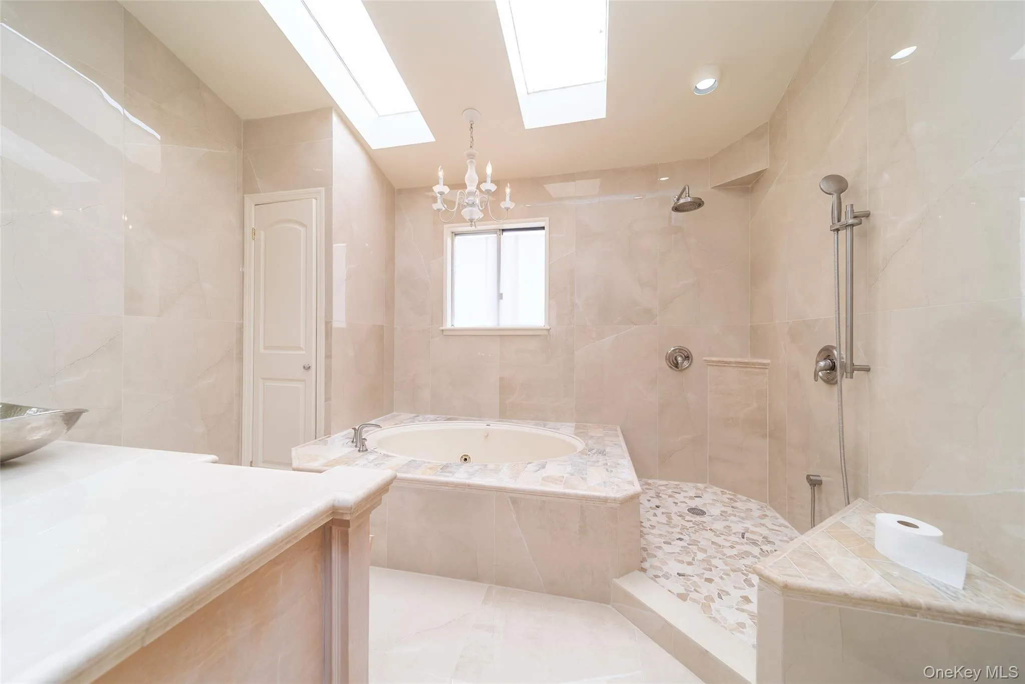 Full bathroom with a whirlpool tub, a skylight, tile walls, tiled shower, and a chandelier Full bathroom with a whirlpool tub, a skylight, tile walls, tiled shower, and a chandelier