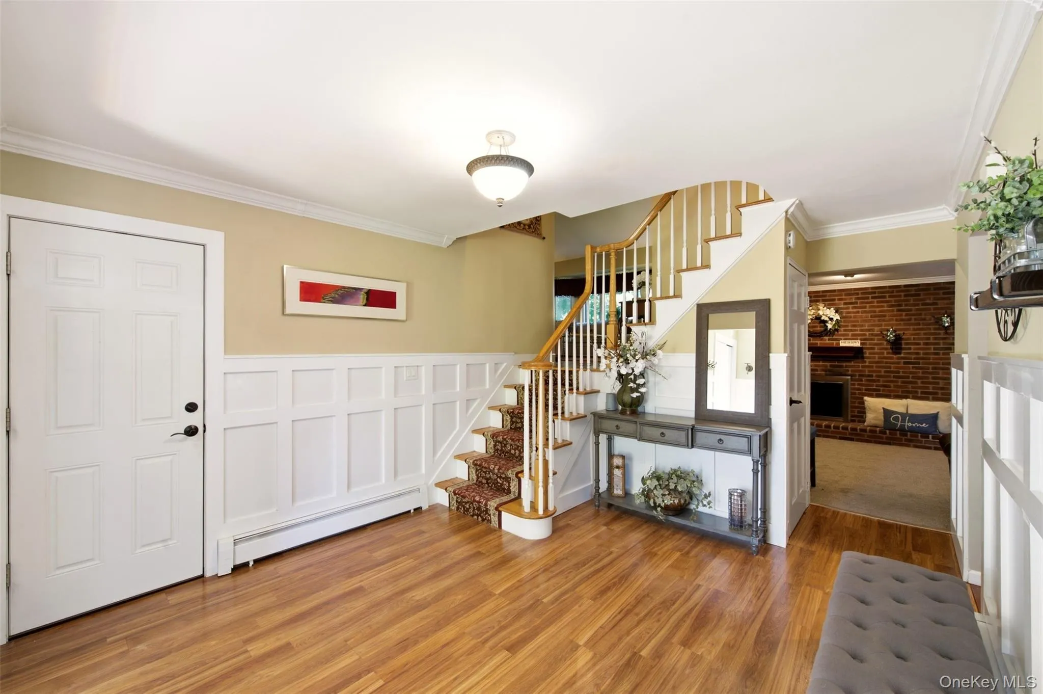Wood-finish flooring throughout, white wainscoting paneling, and a staircase with white balusters and wood handrail Wood-finish flooring throughout, white wainscoting paneling, and a staircase with white balusters and wood handrail