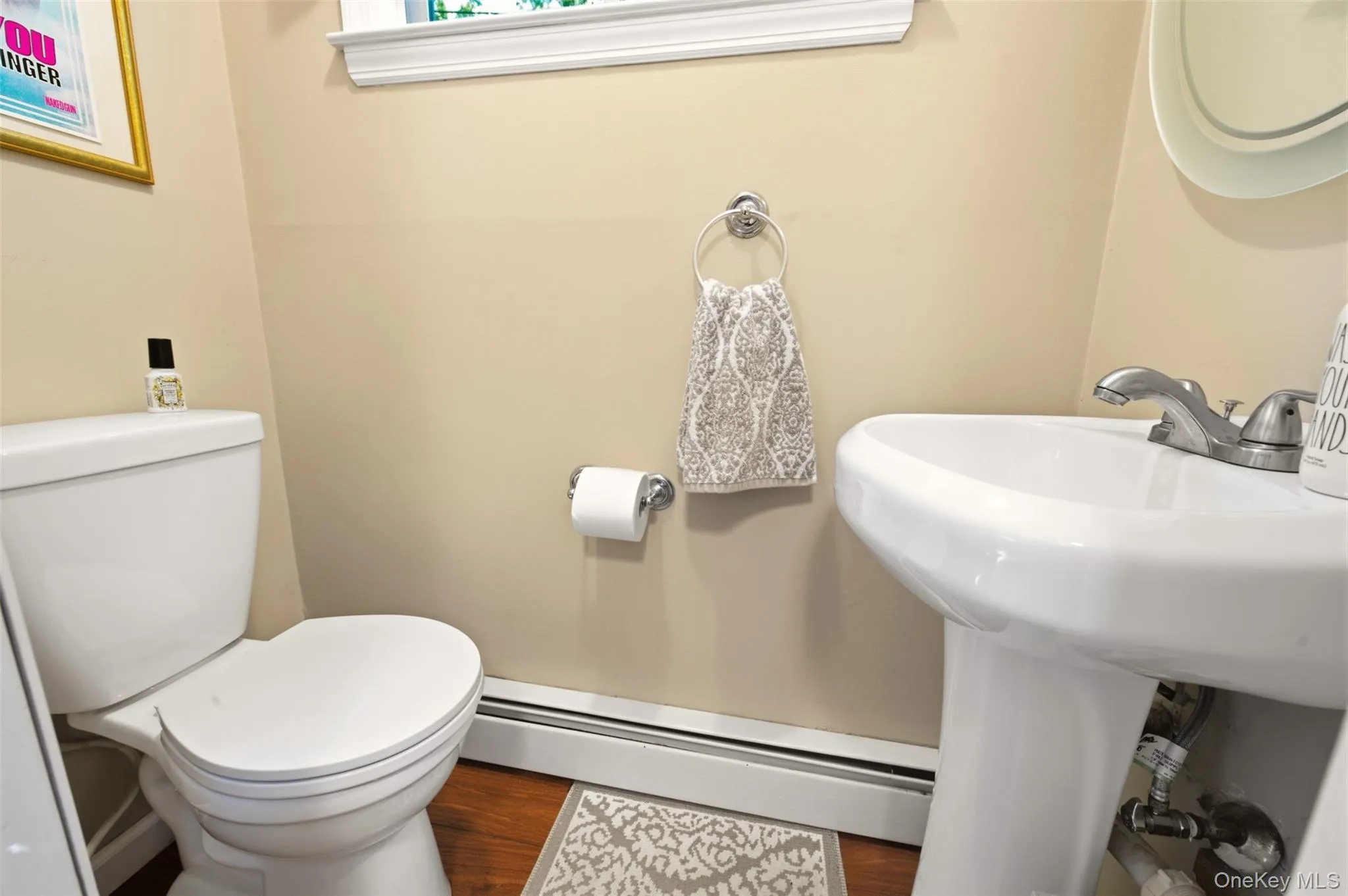 White pedestal sink with chrome faucet, white toilet, wood-finish flooring, and a white window frame with trim White pedestal sink with chrome faucet, white toilet, wood-finish flooring, and a white window frame with trim