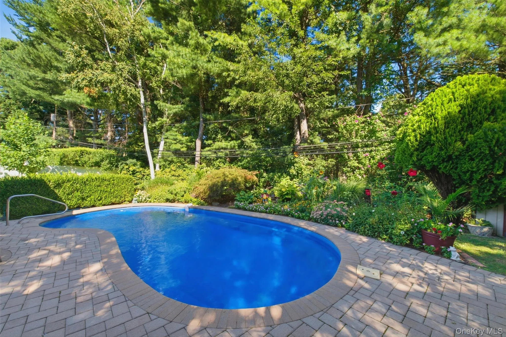 Kidney-shaped in-ground pool with a light blue finish, surrounded by a paver patio with a contrasting border Kidney-shaped in-ground pool with a light blue finish, surrounded by a paver patio with a contrasting border