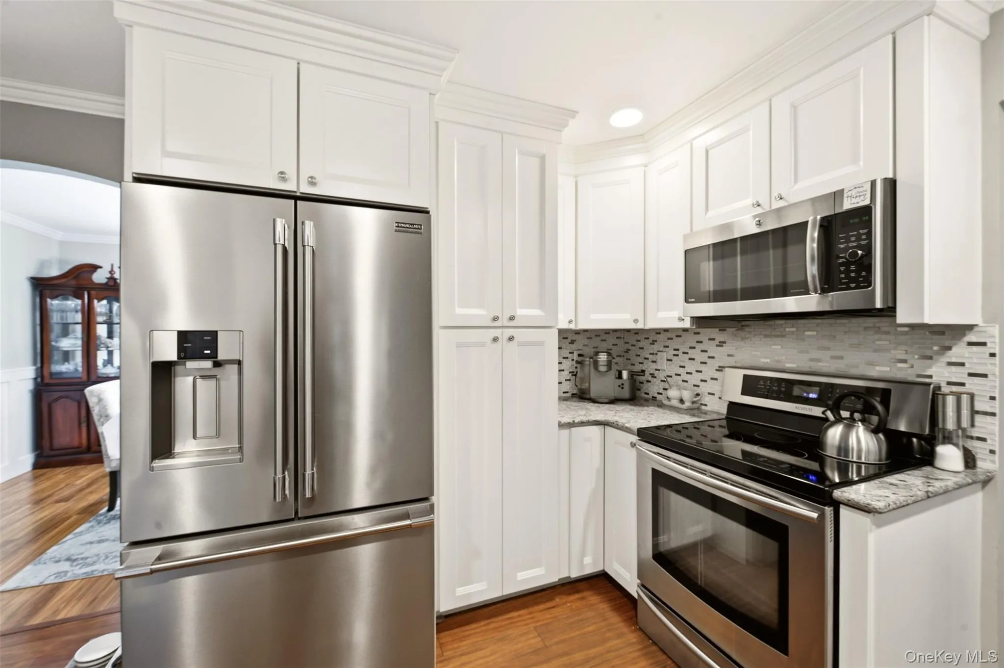 Kitchen featuring stainless steel appliances, white cabinetry, granite countertops, and a mosaic tile backsplash Kitchen featuring stainless steel appliances, white cabinetry, granite countertops, and a mosaic tile backsplash