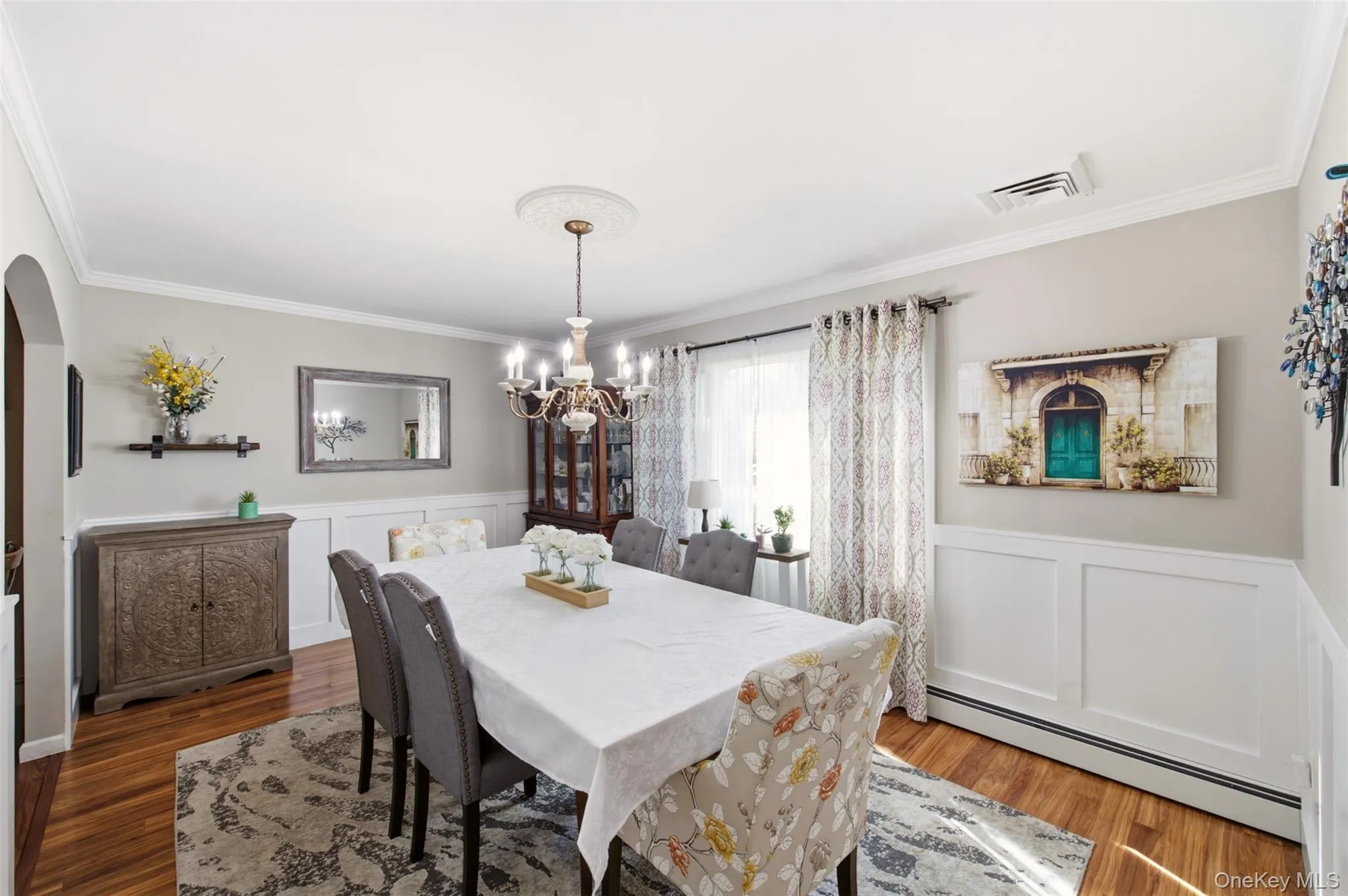 Hardwood flooring, white wainscoting, crown molding, arched entryway, and a chandelier with a ceiling medallion Hardwood flooring, white wainscoting, crown molding, arched entryway, and a chandelier with a ceiling medallion