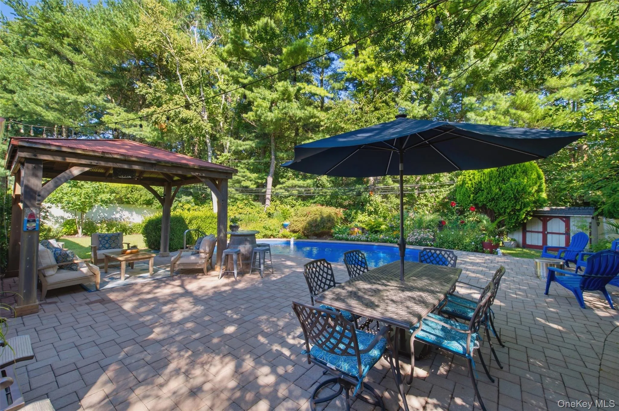 Brick paver patio featuring a wooden gazebo, an in-ground swimming pool, and mature perimeter landscaping Brick paver patio featuring a wooden gazebo, an in-ground swimming pool, and mature perimeter landscaping