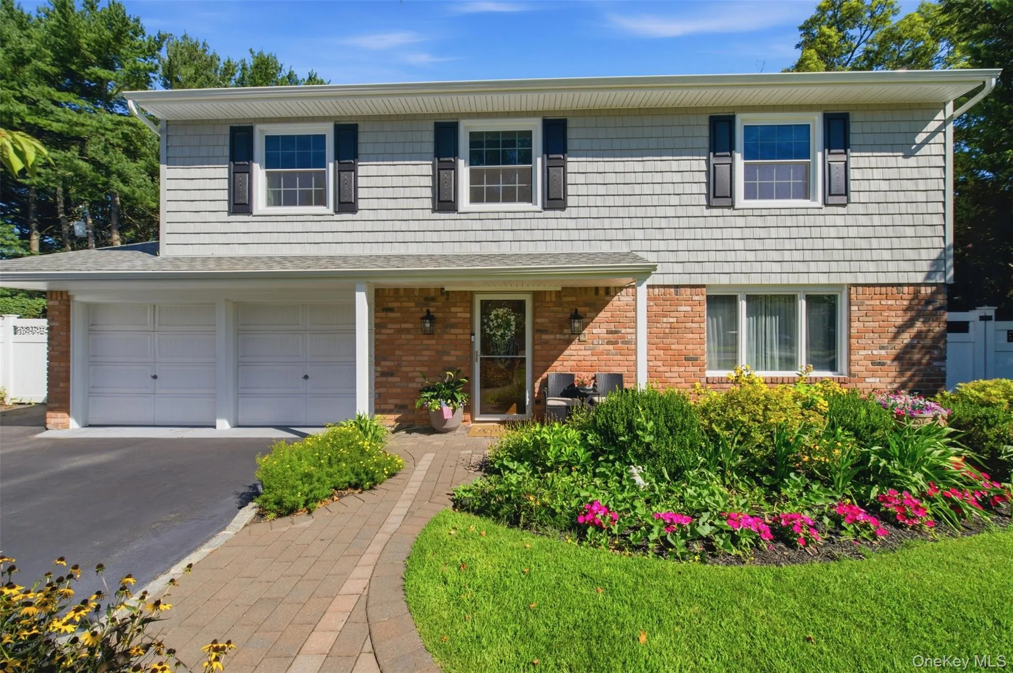 Split-level residence featuring brick and shingle siding, a two-car garage, and a paver walkway Split-level residence featuring brick and shingle siding, a two-car garage, and a paver walkway