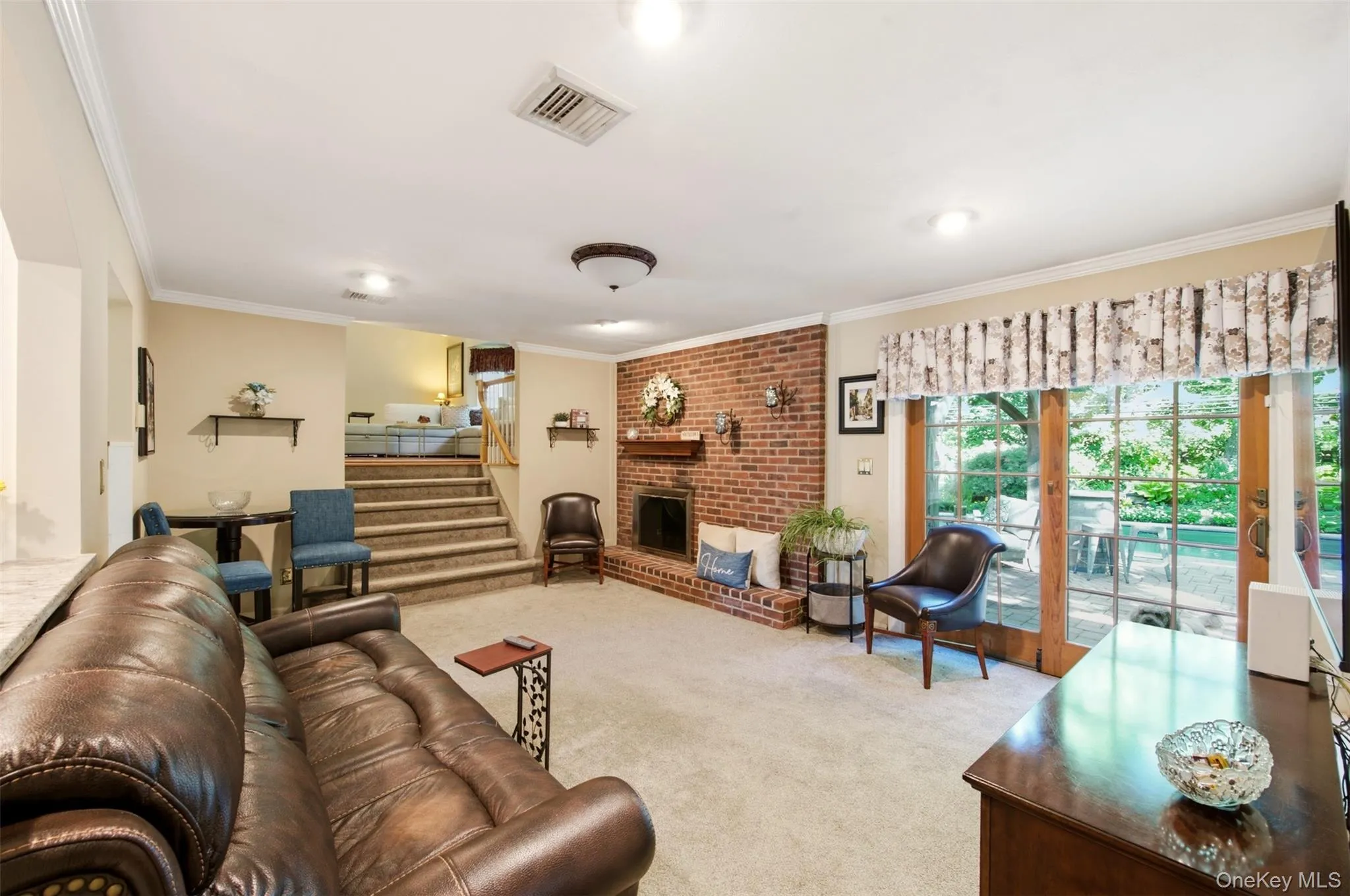 Brick fireplace with a hearth, recessed lighting, crown molding, wood-framed glass patio doors, and a carpeted floor Brick fireplace with a hearth, recessed lighting, crown molding, wood-framed glass patio doors, and a carpeted floor