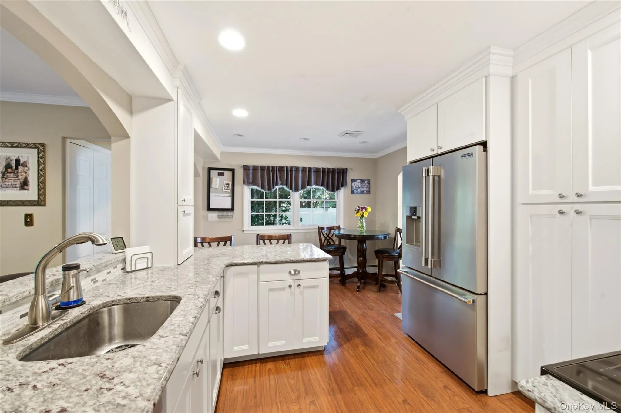 Kitchen featuring white cabinetry, light-colored countertops, a stainless steel refrigerator, and wood-finish flooring Kitchen featuring white cabinetry, light-colored countertops, a stainless steel refrigerator, and wood-finish flooring